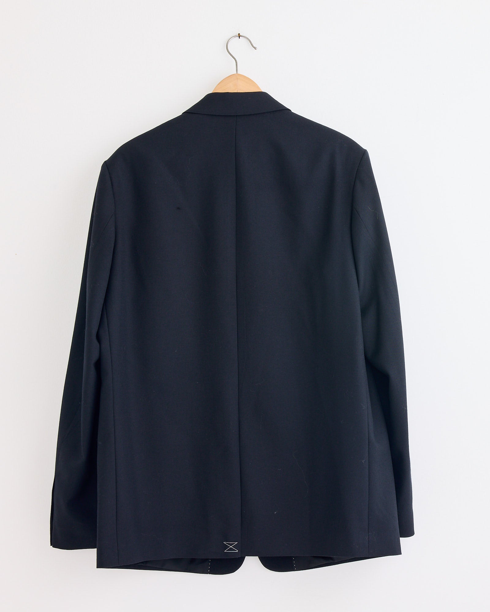 A black blazer from the Dries Van Noten Kiel 2246 Suit hangs on a wooden hanger against a white wall, displayed from the back.
