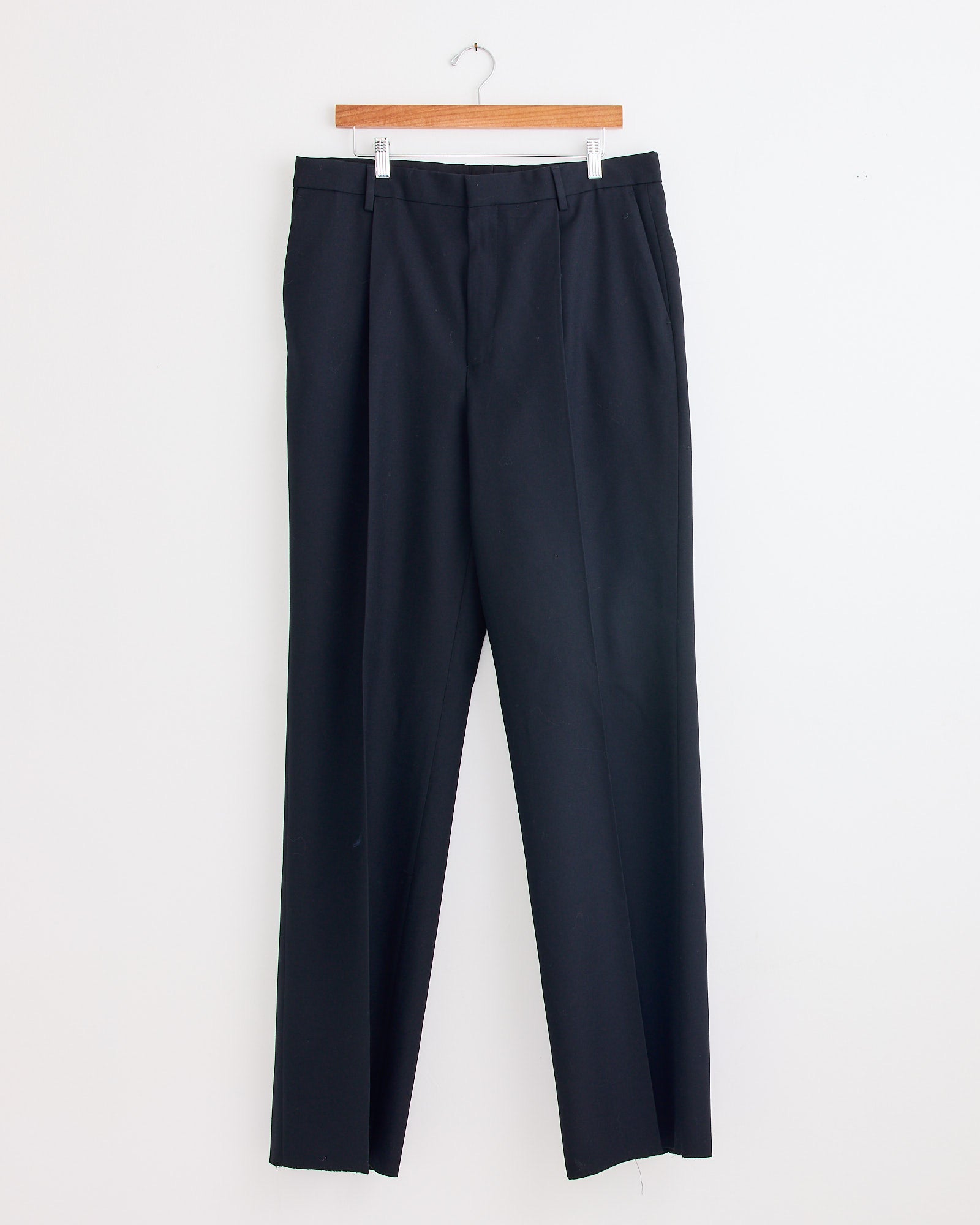 A pair of black wool straight-leg suit pants by Dries Van Noten hangs on a wooden hanger against a white wall, ideal for pairing with the Kiel 2246 Suit in Black or a classic loose fit suit.