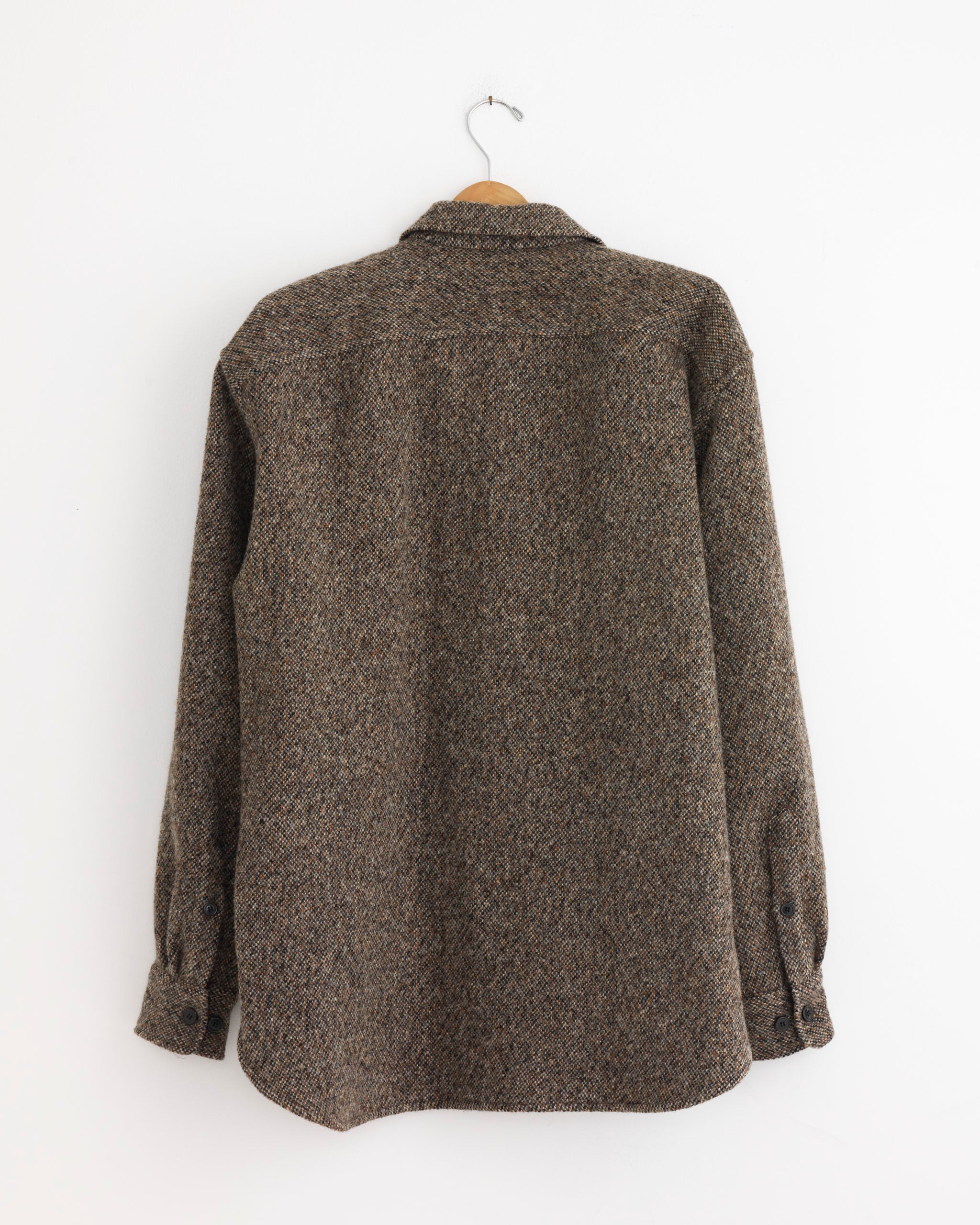 The Dries Van Noten Zip Front Shirt in Rust, featuring long sleeves and textured fabric, is displayed from the back on a wooden hanger against a white wall.