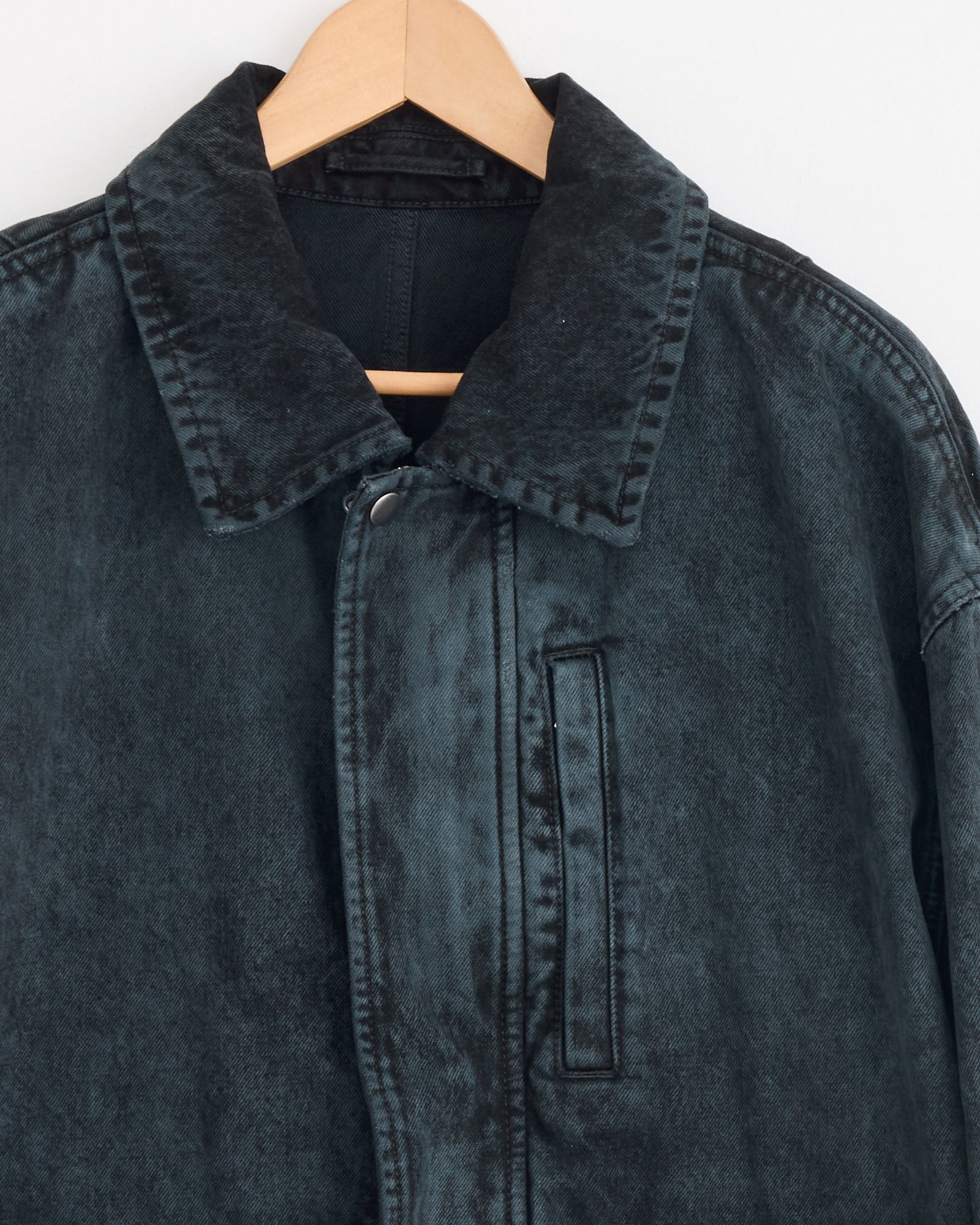 A close-up of Dries Van Noten’s Cotton Jacket in Petrol, featuring its collar, upper section, and vertical chest pocket, hangs on a wooden hanger against a plain white background.