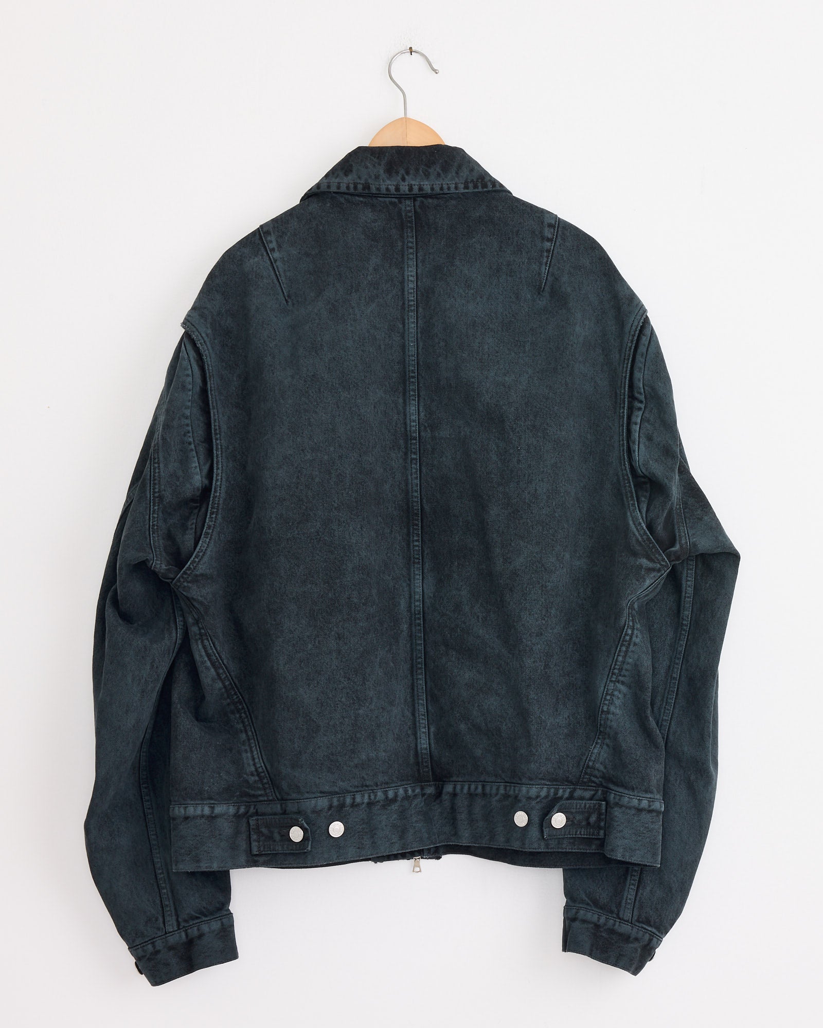 The Cotton Jacket in Petrol by Dries Van Noten hangs on a wooden hanger against a plain white wall, displayed from the back with visible seams, buttons, and cuffs.