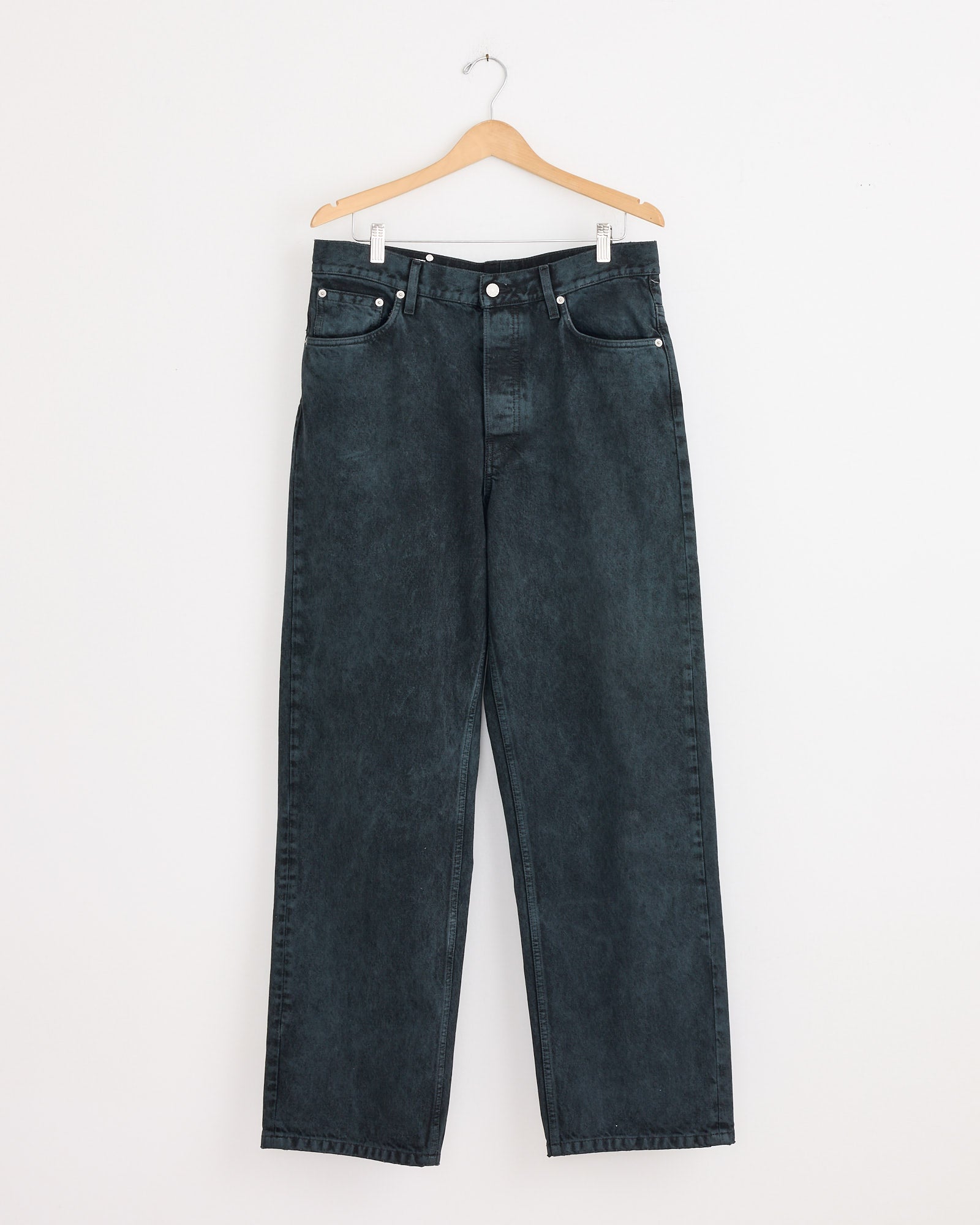 A pair of Loose Fit Jeans in Petrol by Dries Van Noten, made from heavyweight denim with a high waist and straight leg, hangs on a wooden hanger against a plain white wall.