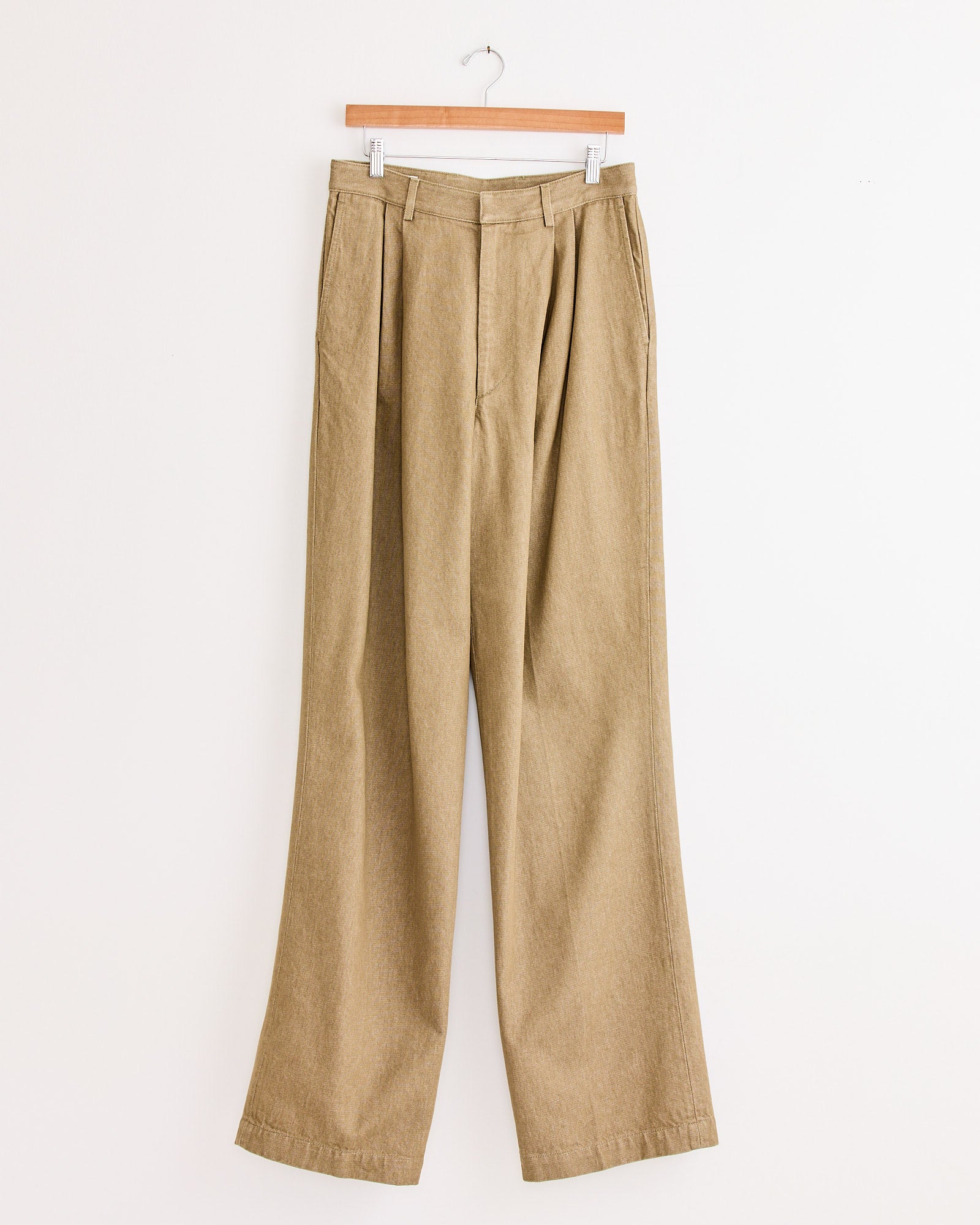 The Pleated Denim Pant in Stone by Dries Van Noten—a wide-leg, high-waisted style with pleats—hangs on a wooden hanger against a plain white background.
