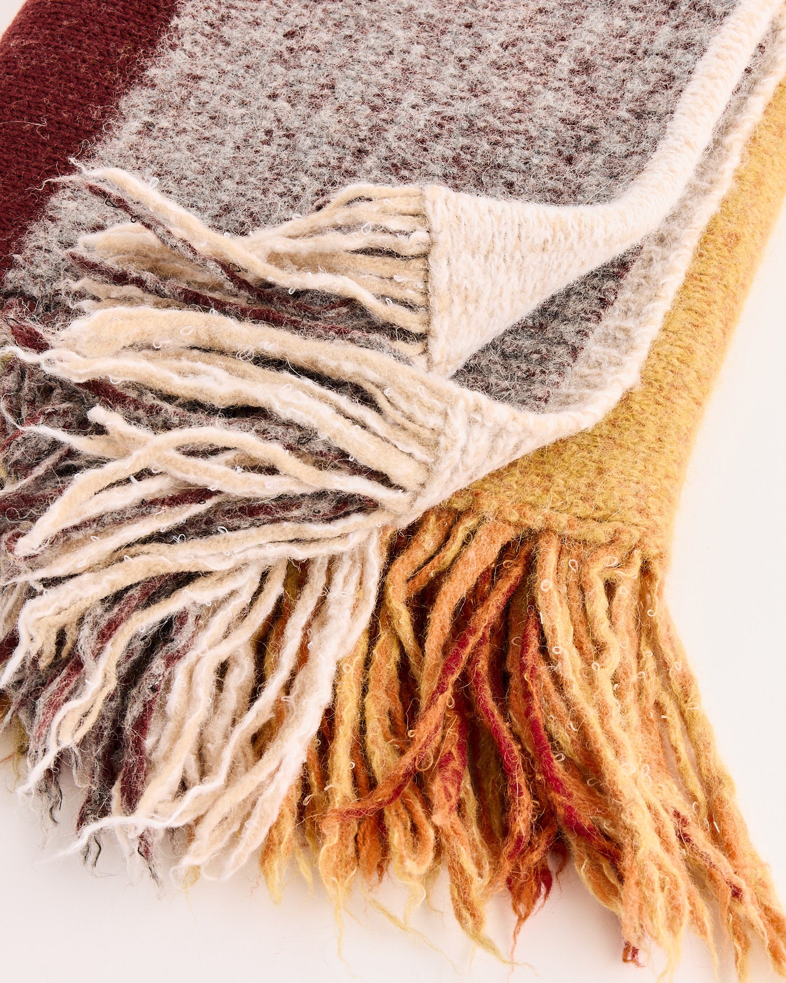 A close-up of the Dries Van Noten Mainly 2725 Scarf in Mustard, a luxurious Italian-made accessory with fringed edges and a gradient of cream, gray, burgundy, and golden yellow in 100% wool.