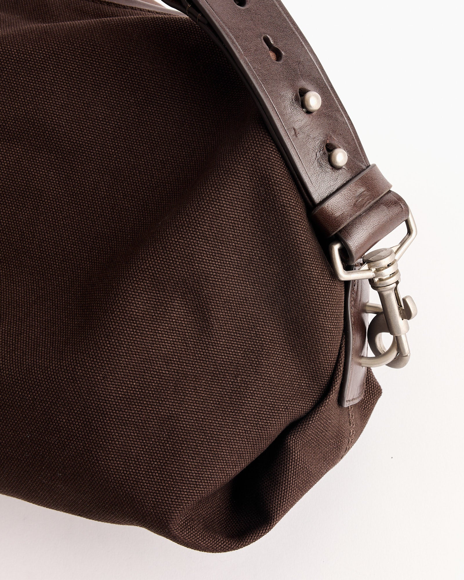 Close-up of the Dries Van Noten Duffle Bag in Dark Brown, featuring cotton material, a dark brown leather strap, and a silver clasp, made in Italy, shown against a plain white background.