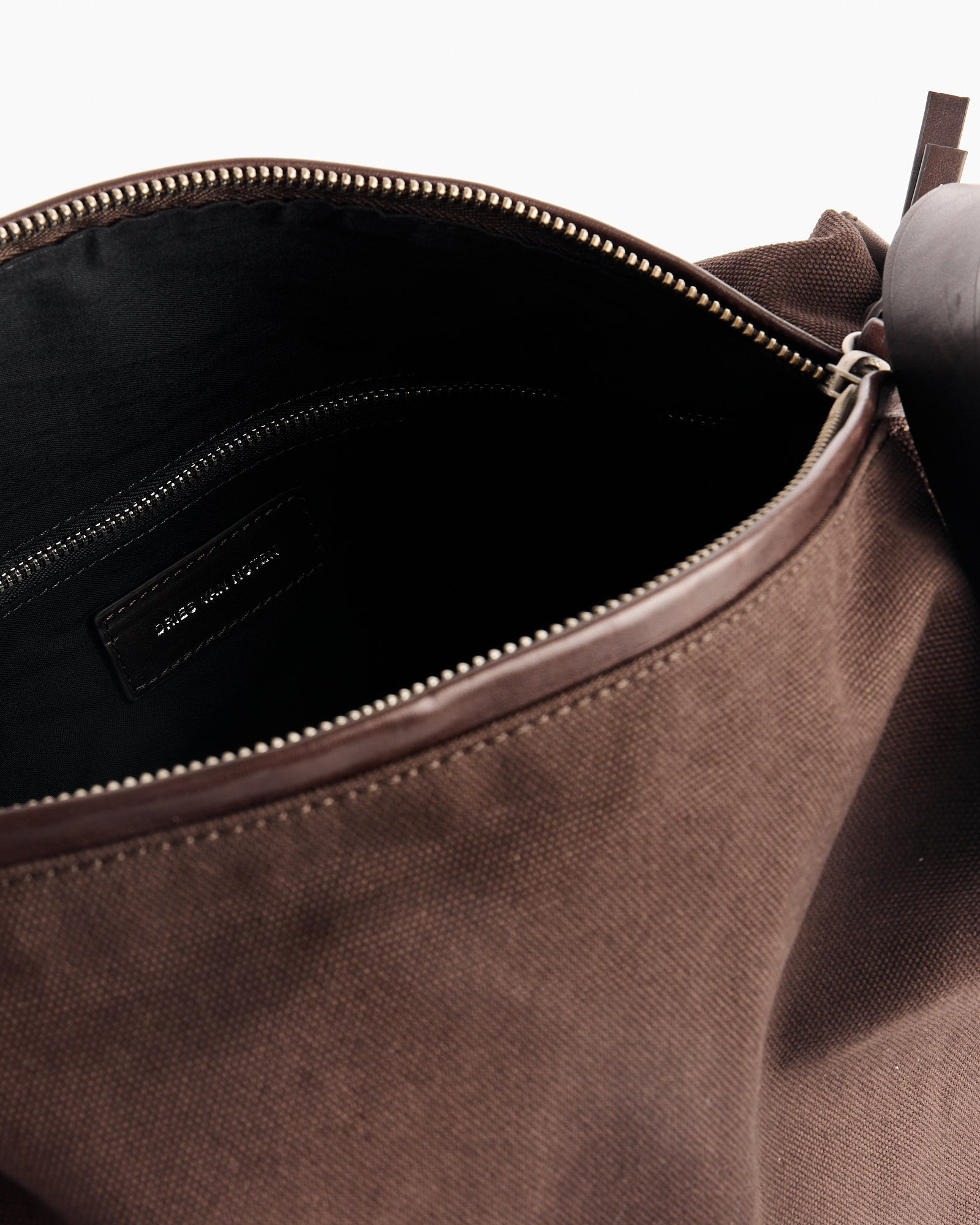 Close-up of an open Dries Van Noten Duffle Bag in Dark Brown, featuring a leather zipper, dark cotton interior, and a stitched label inside.
