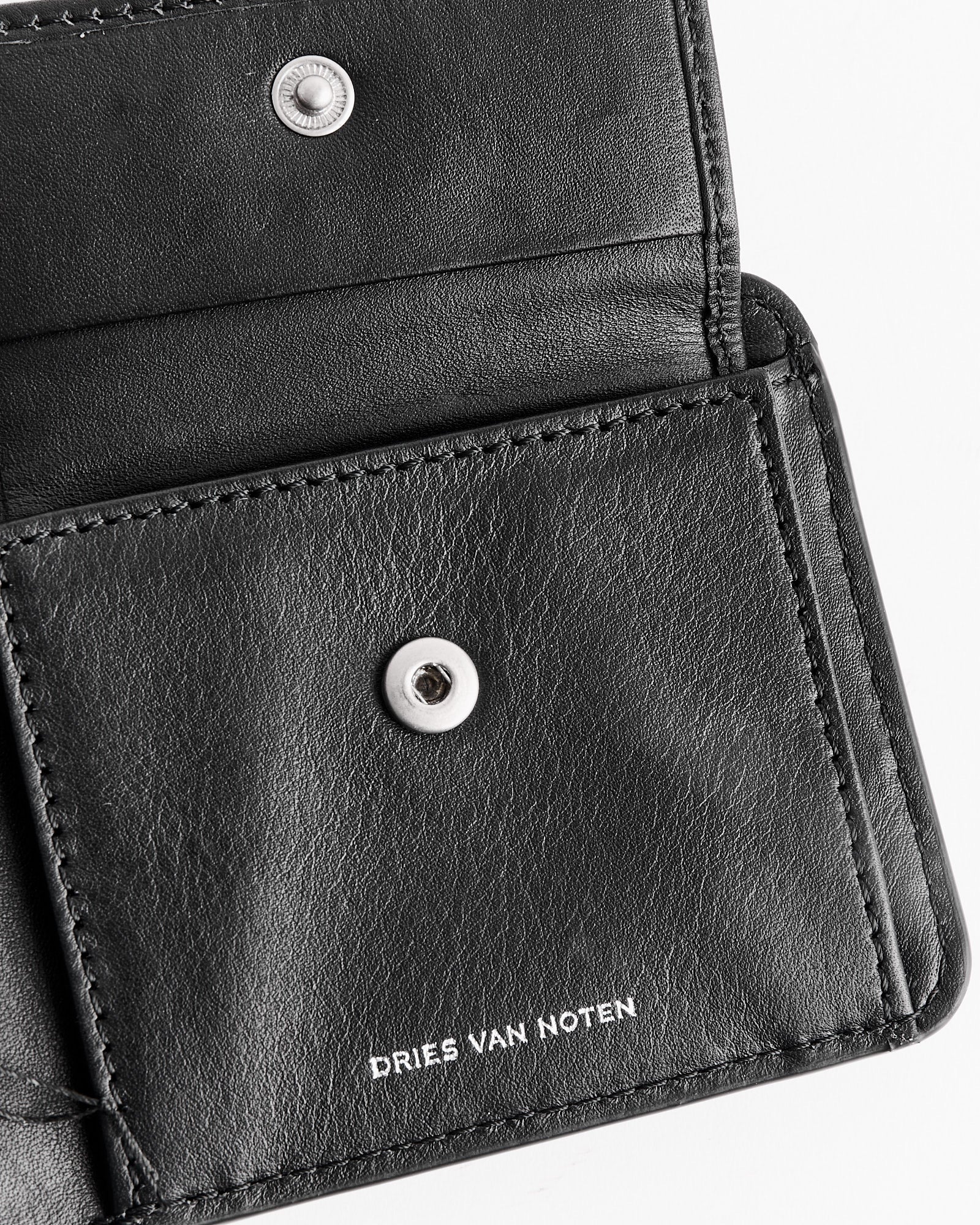 A close-up of an open Dries Van Noten 995-151 Wallet in black, featuring silver snap buttons and the brand name embossed in white.