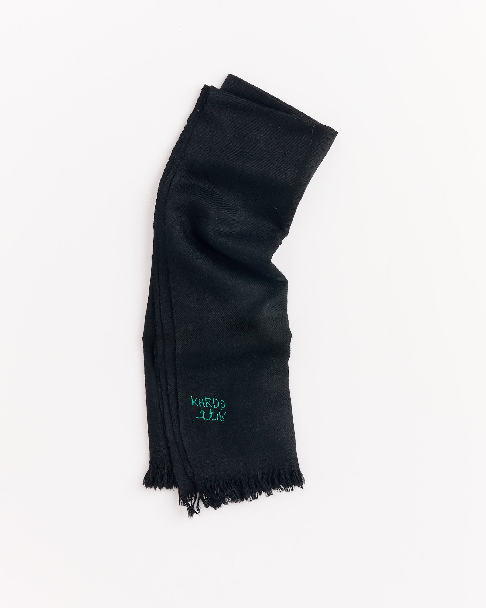 The Handwoven Pashmina Bandana in Black by Kardo is shown folded on a white background, featuring short fringe at both ends and green Kardo embroidery near the edge.