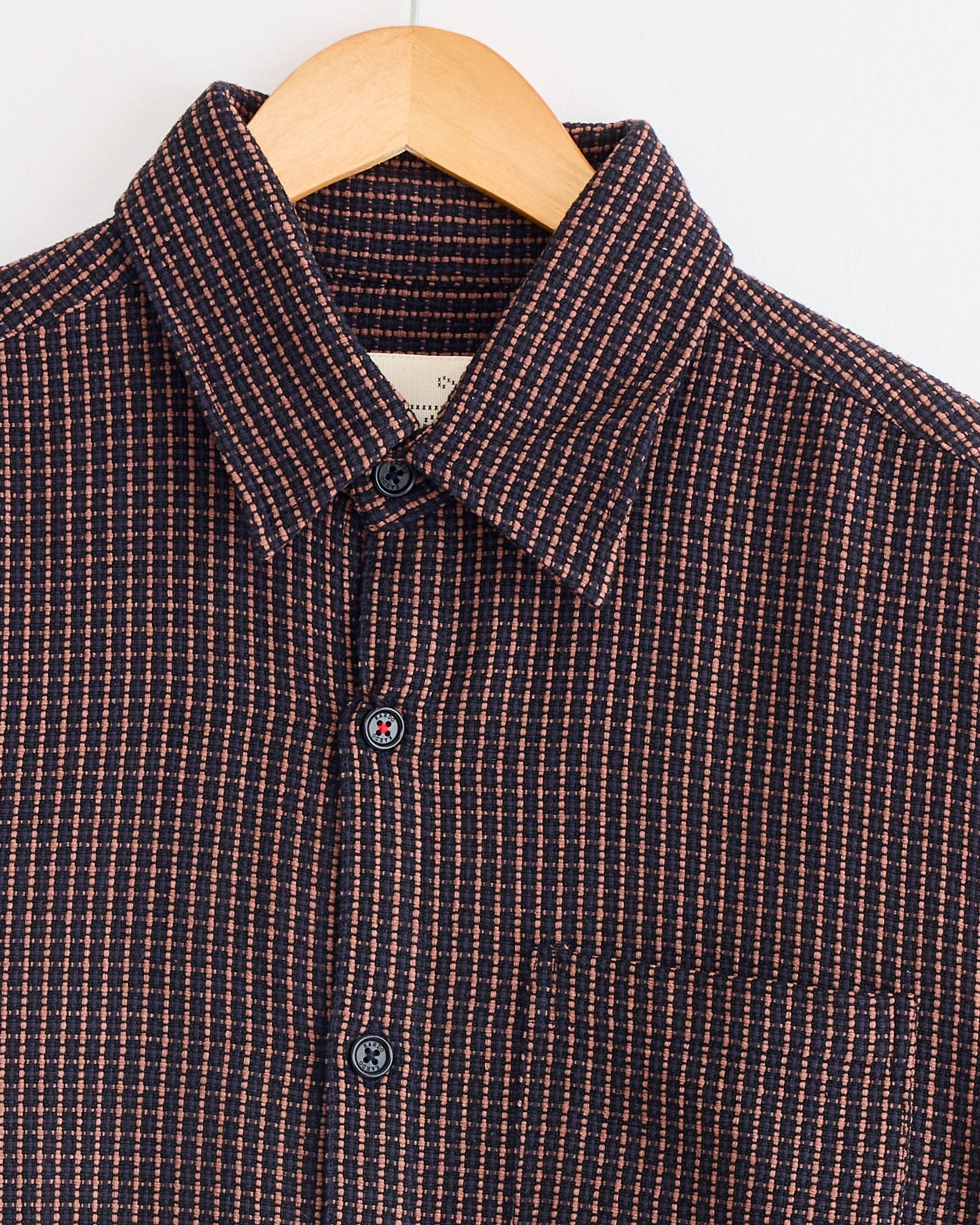 The Kardo Luis Shirt in Ganache, featuring a small navy blue and red geometric checkered pattern, is shown on a wooden hanger against a plain white background.