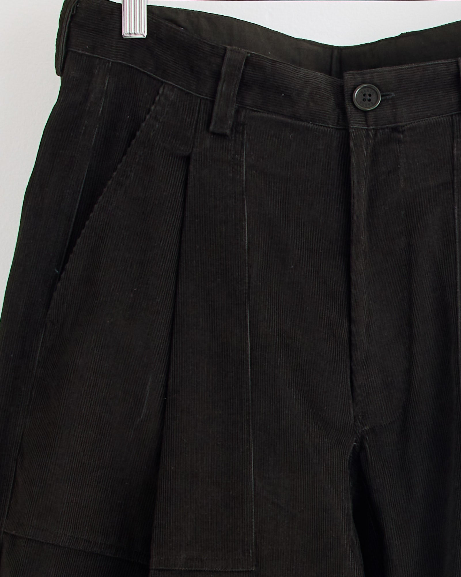Close-up of Kardo’s Yuki Trouser in Dark Green hanging on a hanger, highlighting the waistband, button, belt loop, and side pocket details. For sizing or fit questions, our online chat is here to help.