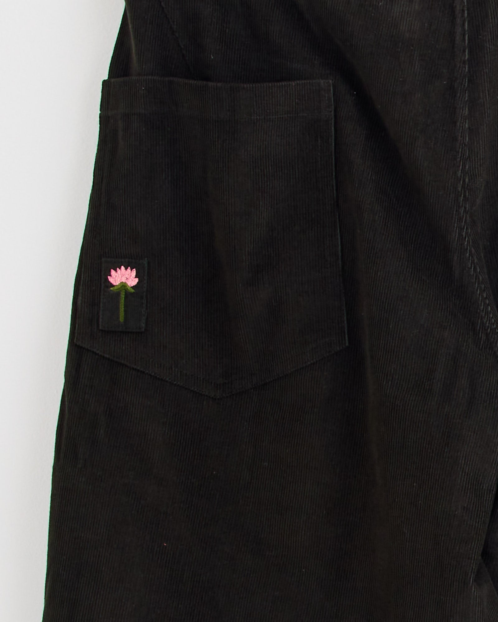 A close-up of the Kardo Yuki Trouser in Dark Green shows a corduroy pocket with a black patch embroidered with a pink flower and green stem. For fit or sizing questions, chat with our online team.