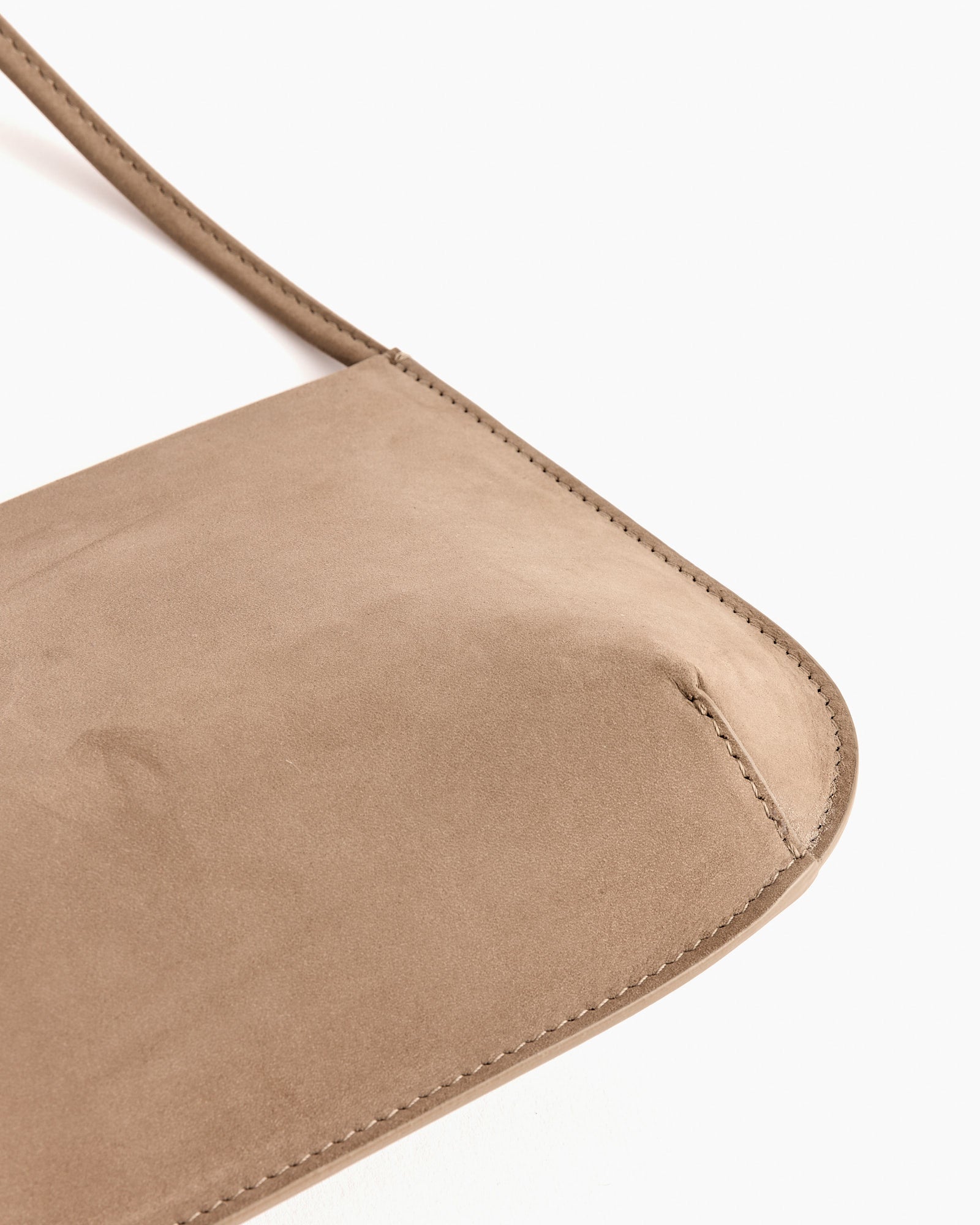Close-up of the FANE Bra Bag in Biche, crafted from beige suede with precise edge stitching and a smooth, rounded corner—part of the strap is visible. Contact our online chat for advice on fit or sizing.
