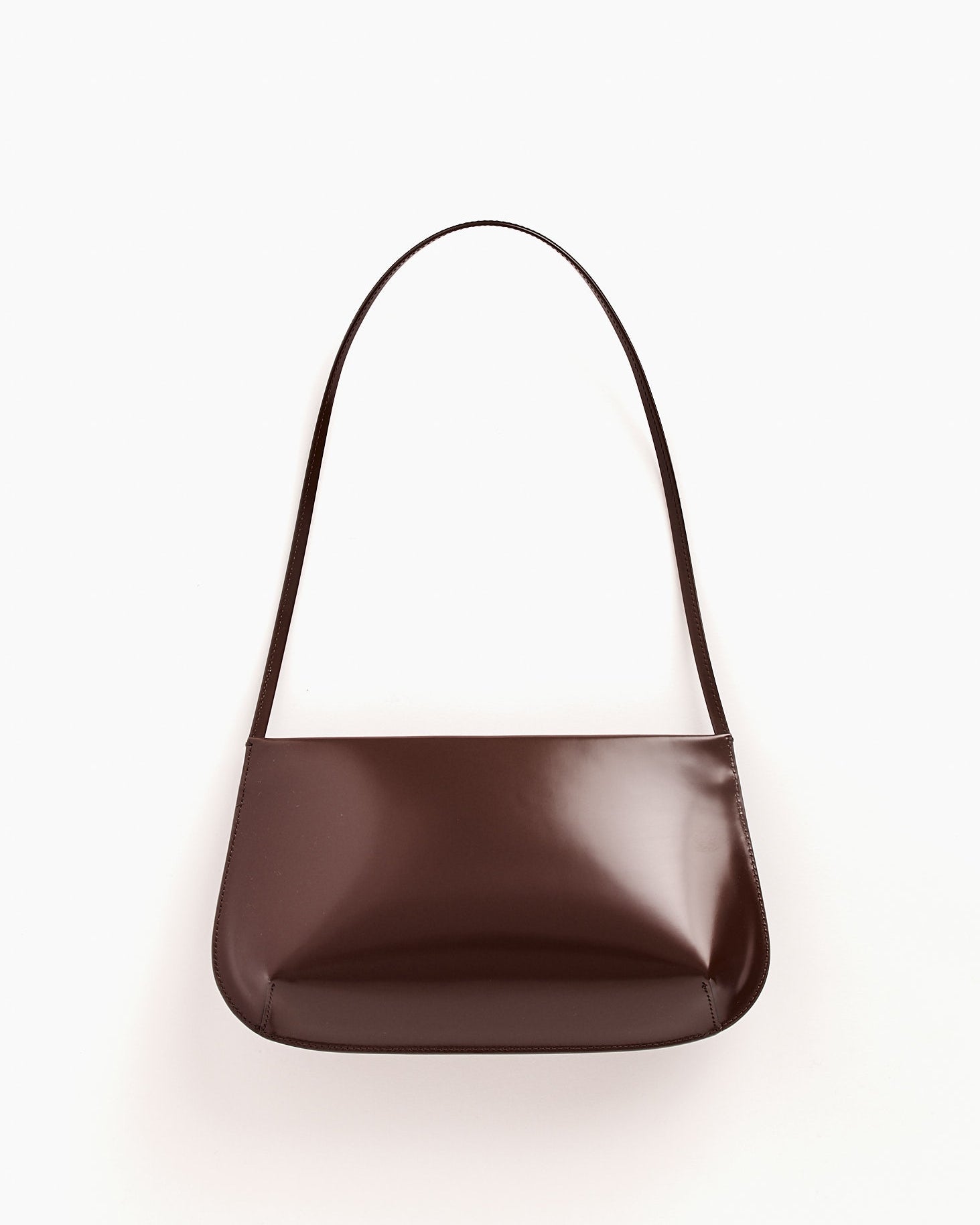 The Bra Bag in Choc by FANE is a minimalist, glossy dark brown Italian spazzolato leather shoulder bag with a single strap, shown against a plain white background.