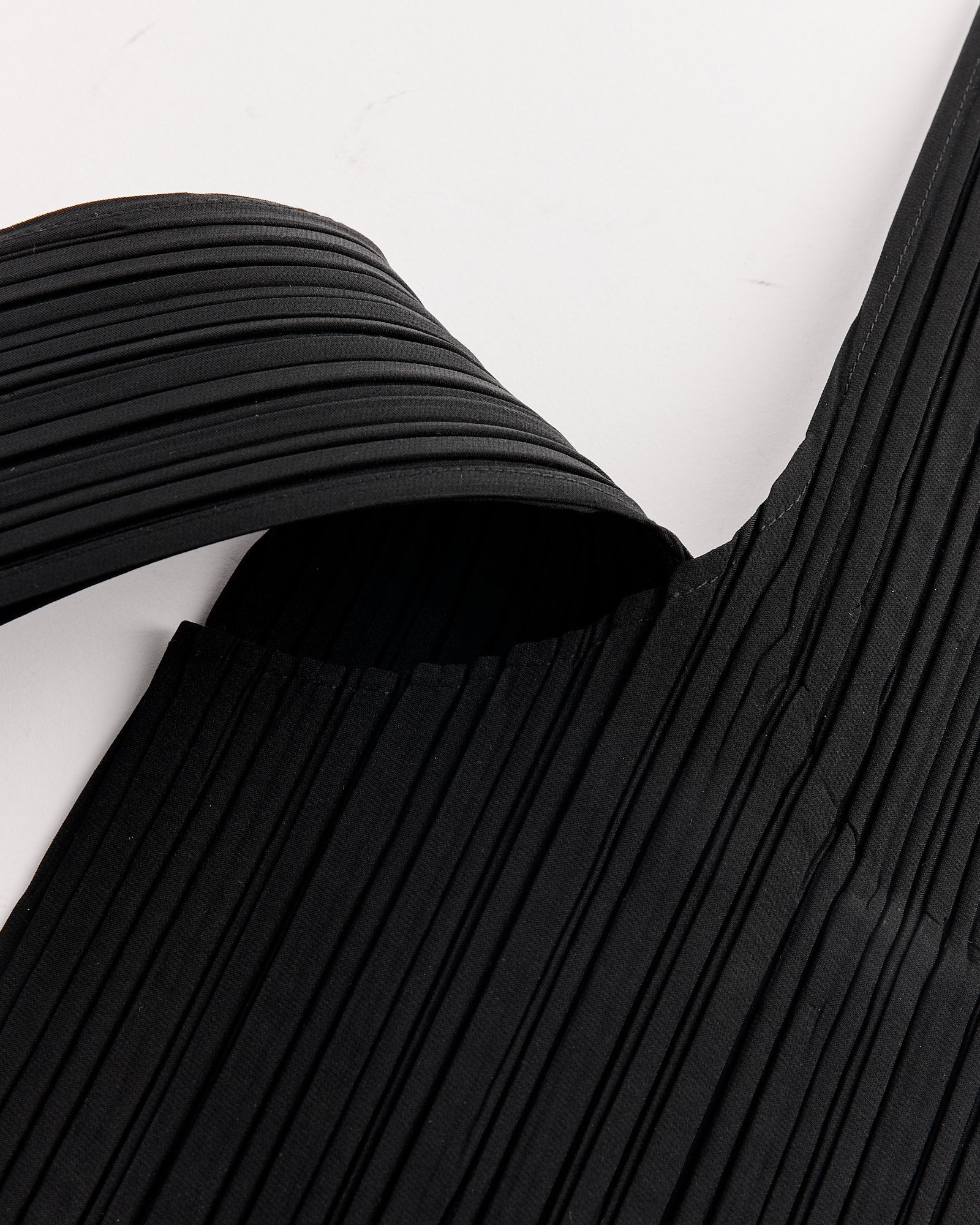 Close-up of the Shift Pleats Bag in Black by Pleats Please Issey Miyake, featuring black pleated fabric and a wide, textured strap. For questions about sizing or fit, contact us via online chat.