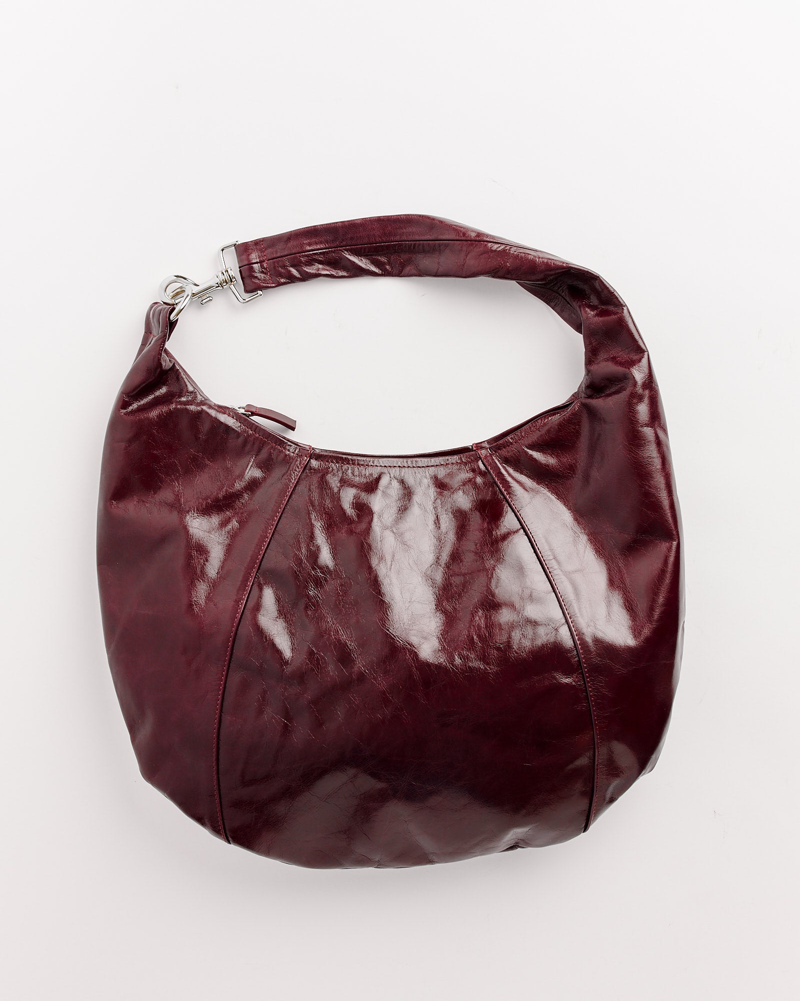 The Paula Bag in Burgundy by Gimaguas features glossy dark burgundy leather, a rounded shape, and a single short handle. Shown on a plain white background. For fit or sizing questions, our online chat support is ready to help.
