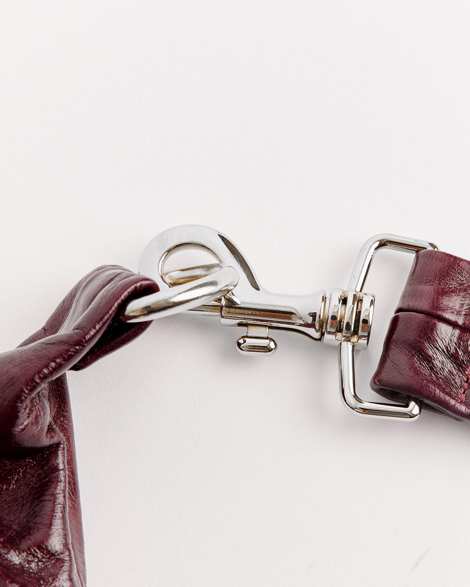 Close-up of a shiny silver clasp on the glossy burgundy leather strap of the Gimaguas Paula Bag, set against a white background—contact our online chat for questions about sizing or fit.