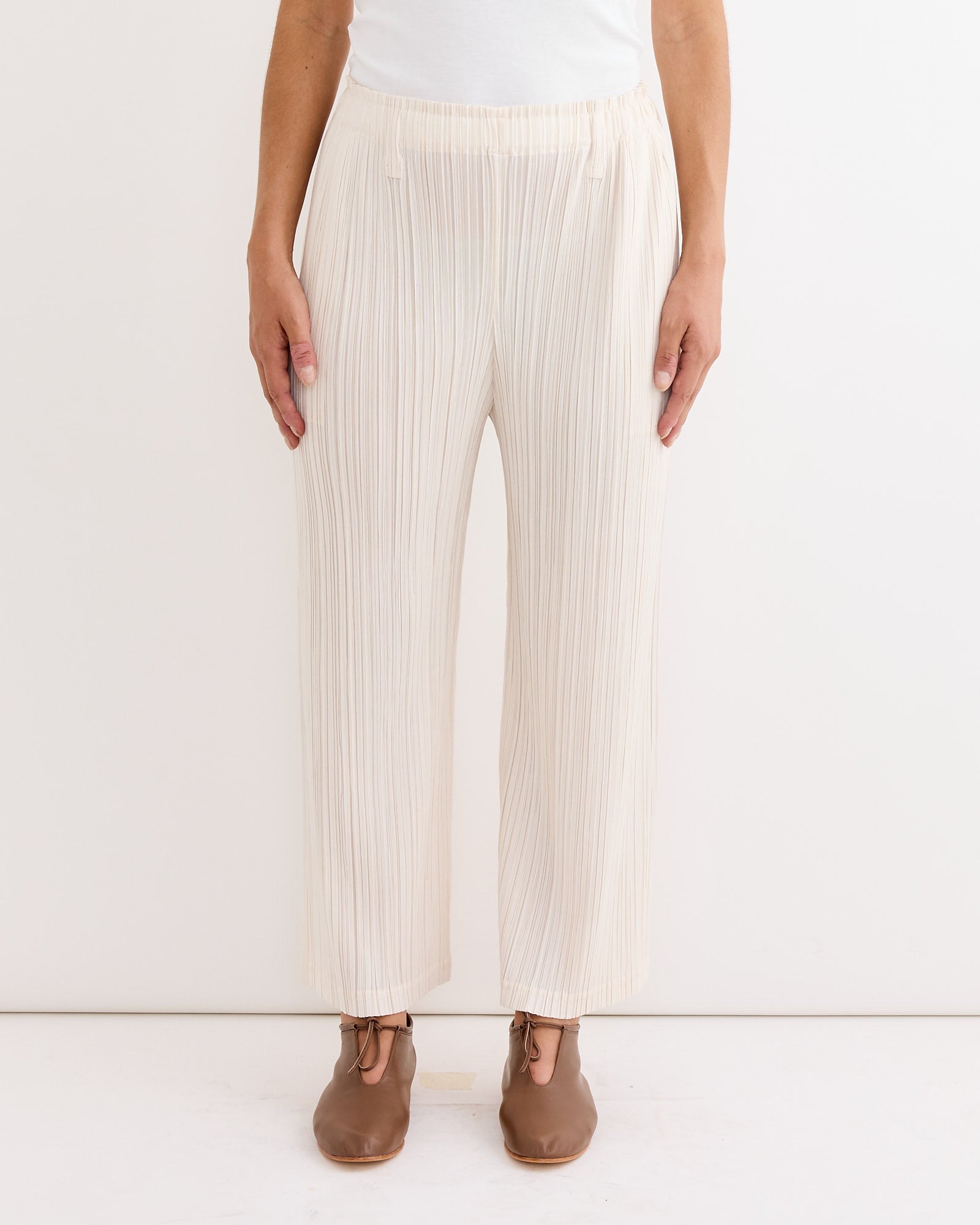 A person wears Pleats Please Issey Miyake Thicker Bottoms 2 Pant in Off White with brown lace-up shoes, standing against a plain white background. Only the lower half of the body is visible.