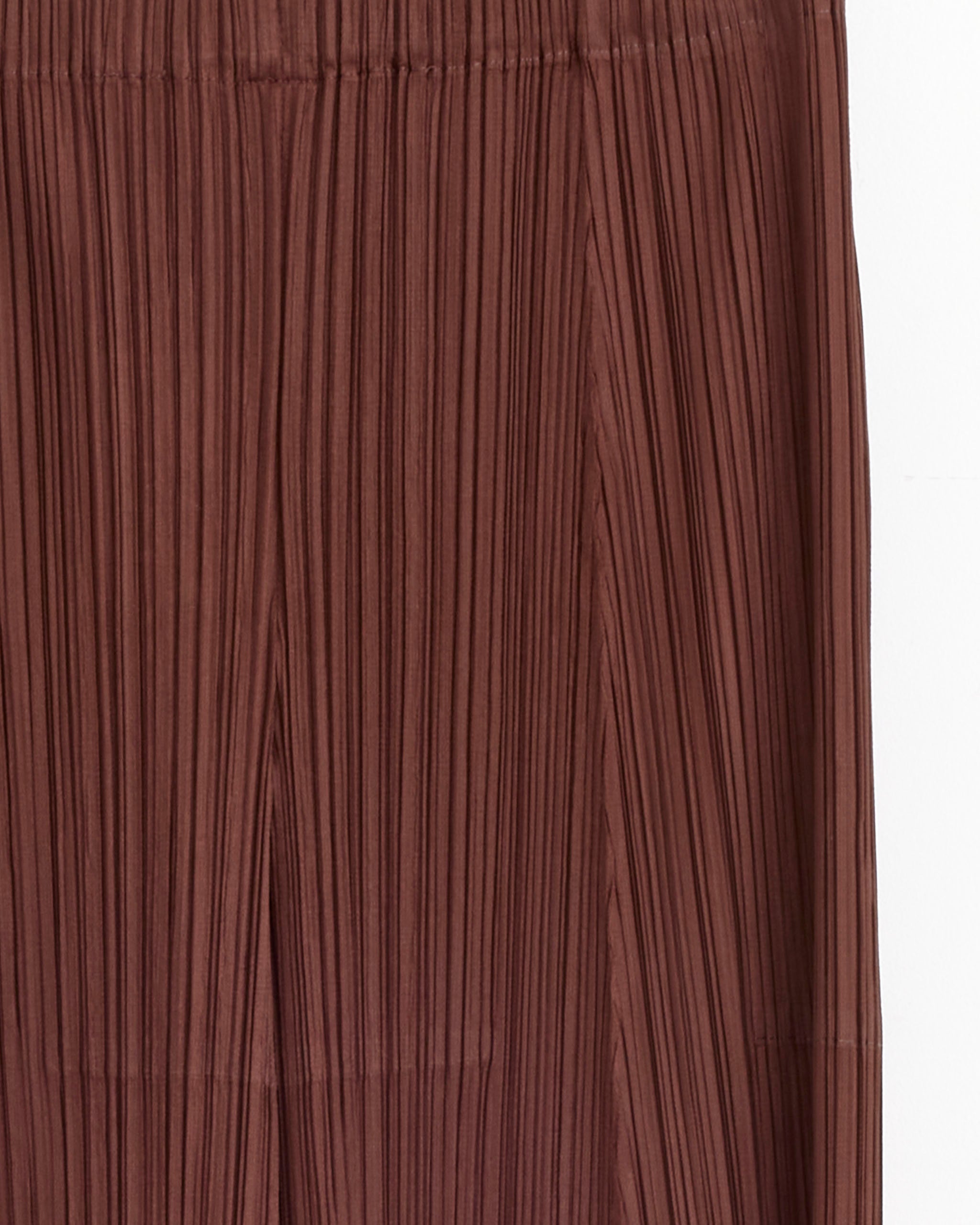 Close-up of the Nov Pant in Brown by Pleats Please Issey Miyake, featuring pleated fabric with vertical lines and a gathered waistband for comfort. For sizing questions, our online chat is here to help.