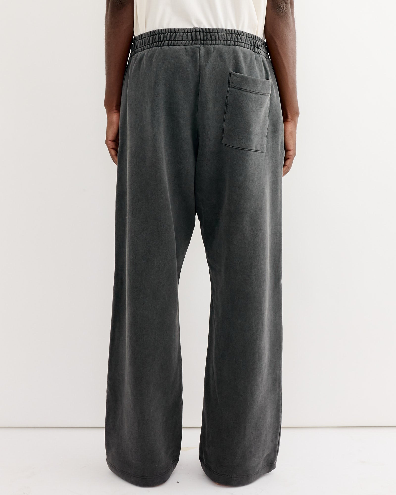 A person wearing the SMOCK Veloso Pant in 22oz French Terry Grey, featuring an elastic waistband and single back pocket, stands against a plain white background, shown from the back. Expertly made in Los Angeles.