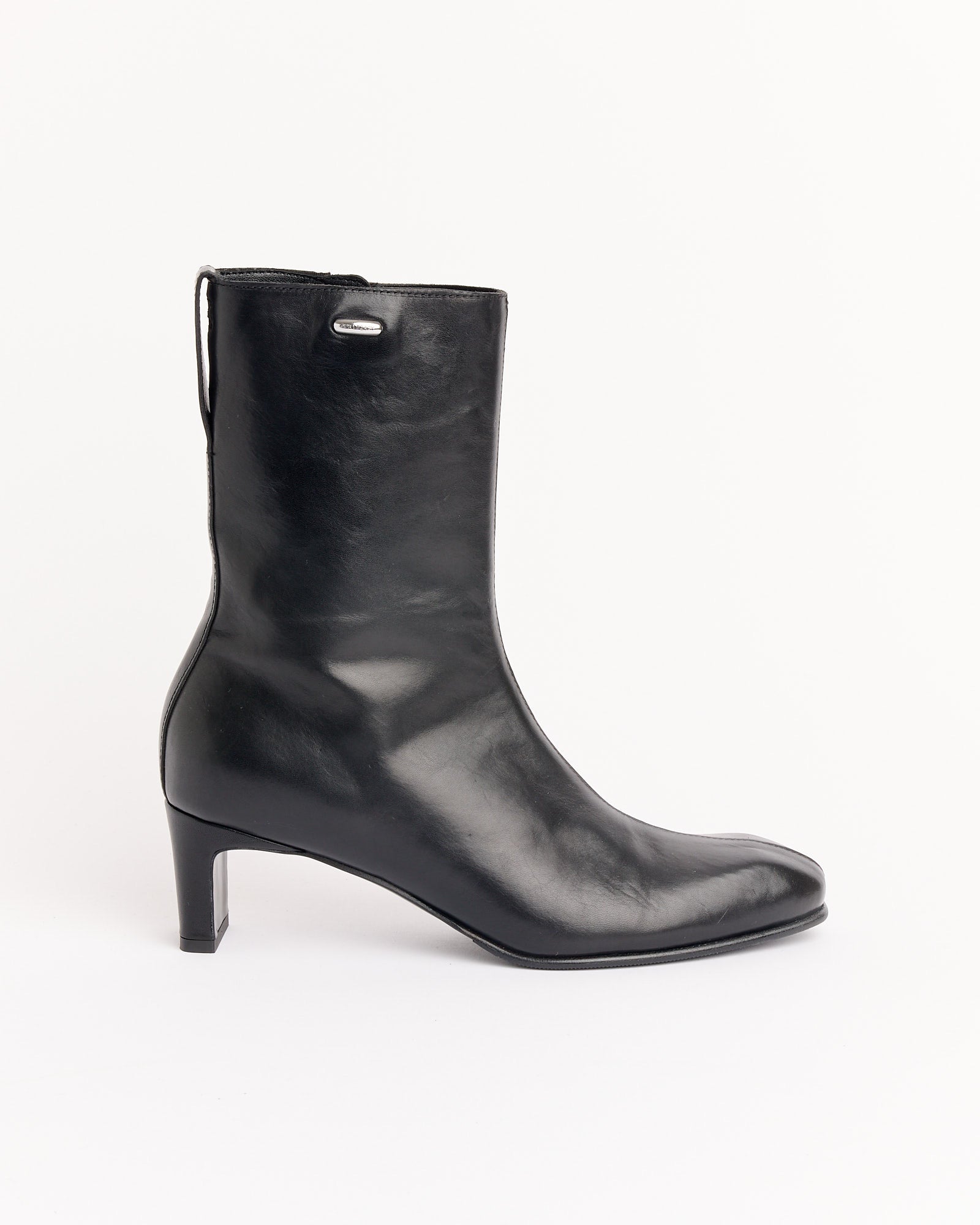 The Karasu Heel Boot in Black by Our Legacy is a single black leather boot with a mid-heel, rounded toe, and pull loop at the back, shown against a plain white background.