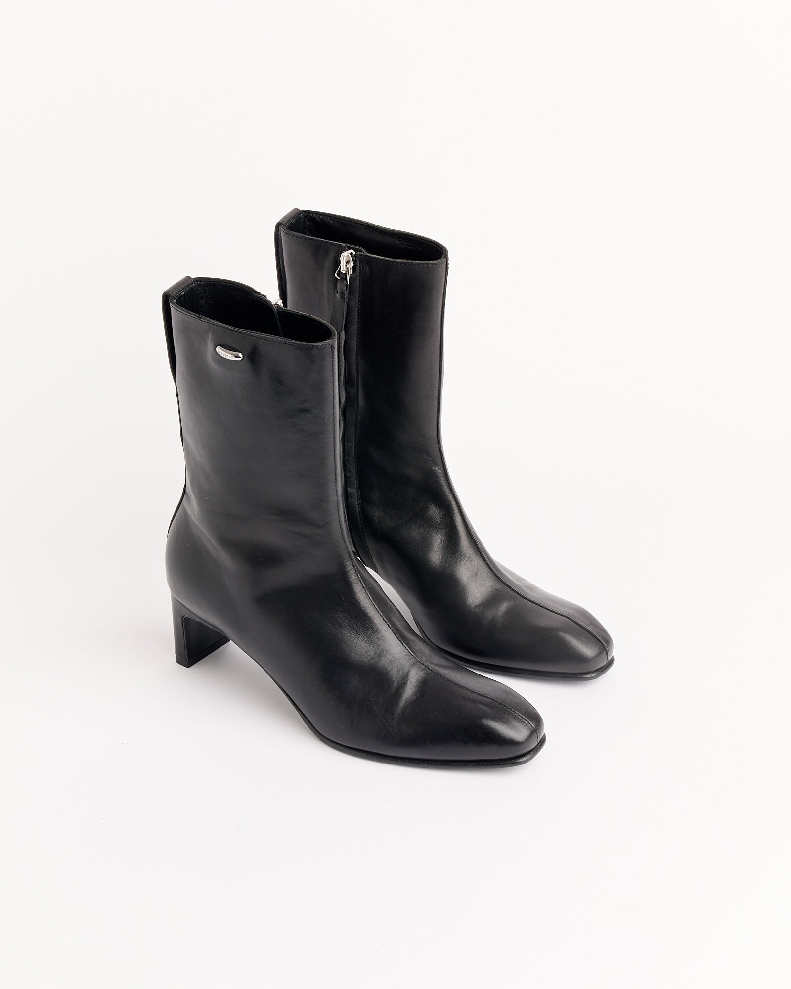 The Our Legacy Karasu Heel Boot in Black is a pair of black leather mid-calf boots with side zippers and low block heels, shown on a white background.