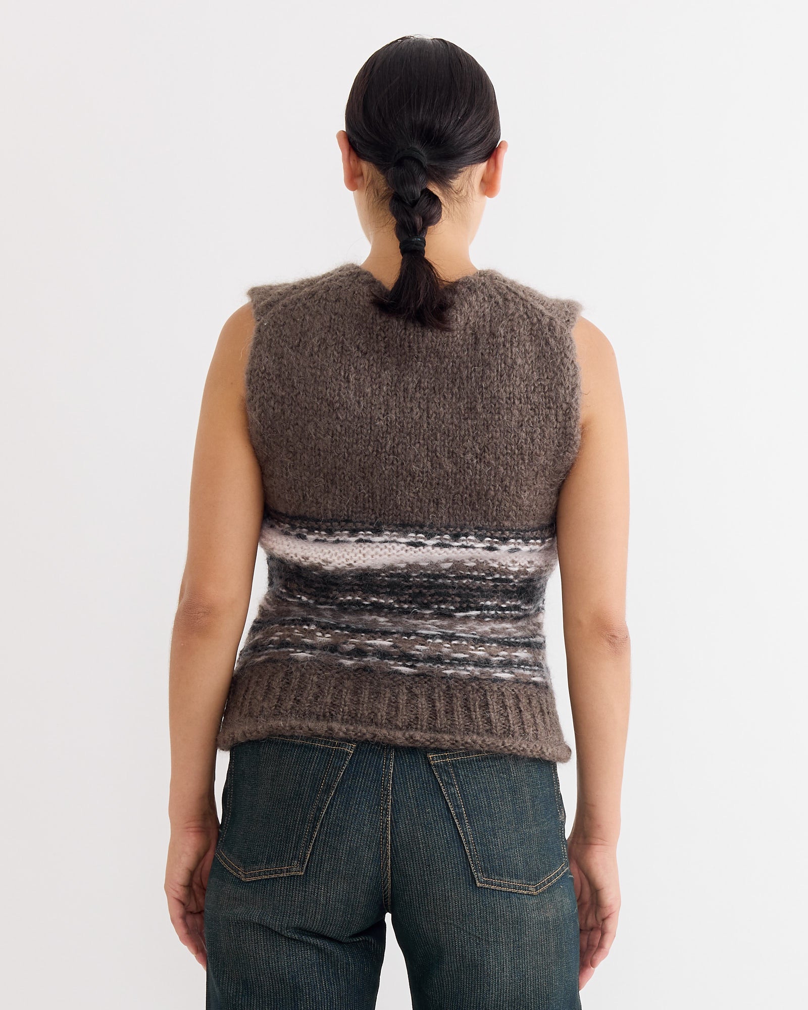 A person with dark braided hair is shown from the back, wearing the Our Legacy Pleaser Tank in Blur Fair Isle and dark blue jeans, standing against a plain white background.