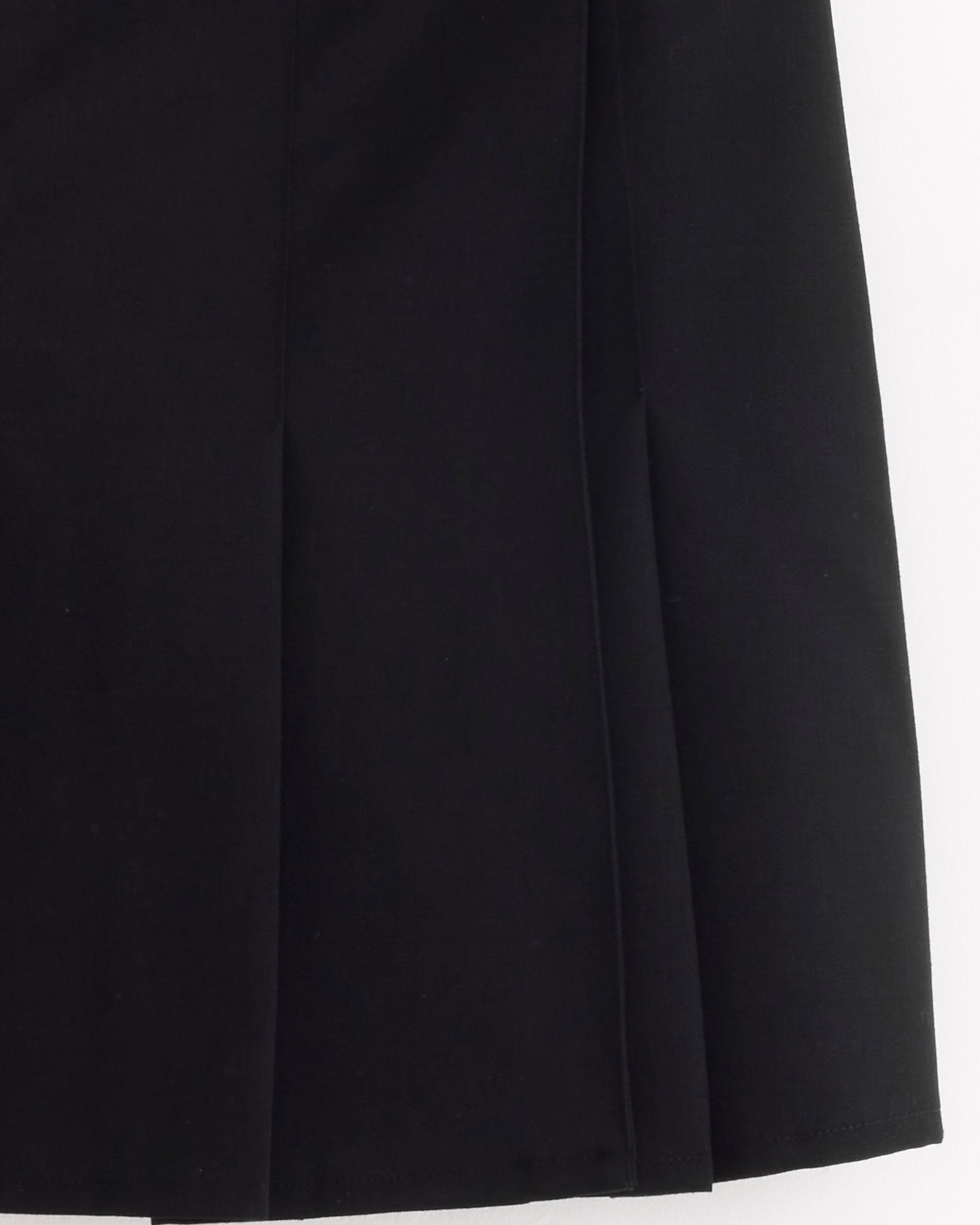 A close-up of Our Legacy’s Girdle Skirt in Coarse Black Gabardine highlights two vertical pleats and the smooth fabric texture. Part of the A-line silhouette appears against a clean white background.
