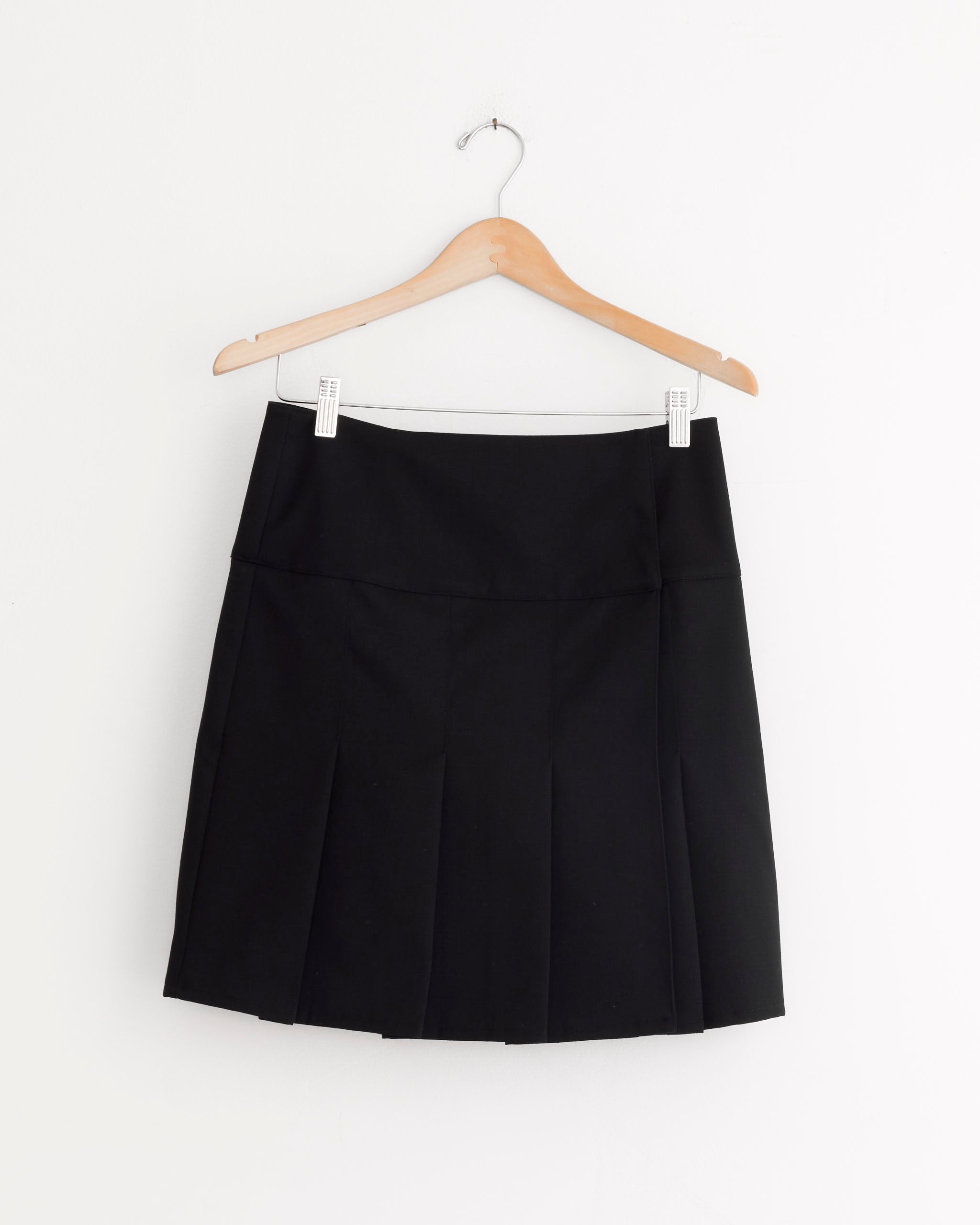 The Girdle Skirt in Coarse Black Gabardine by Our Legacy, featuring an A-line silhouette, hangs on a wooden hanger against a plain white wall.
