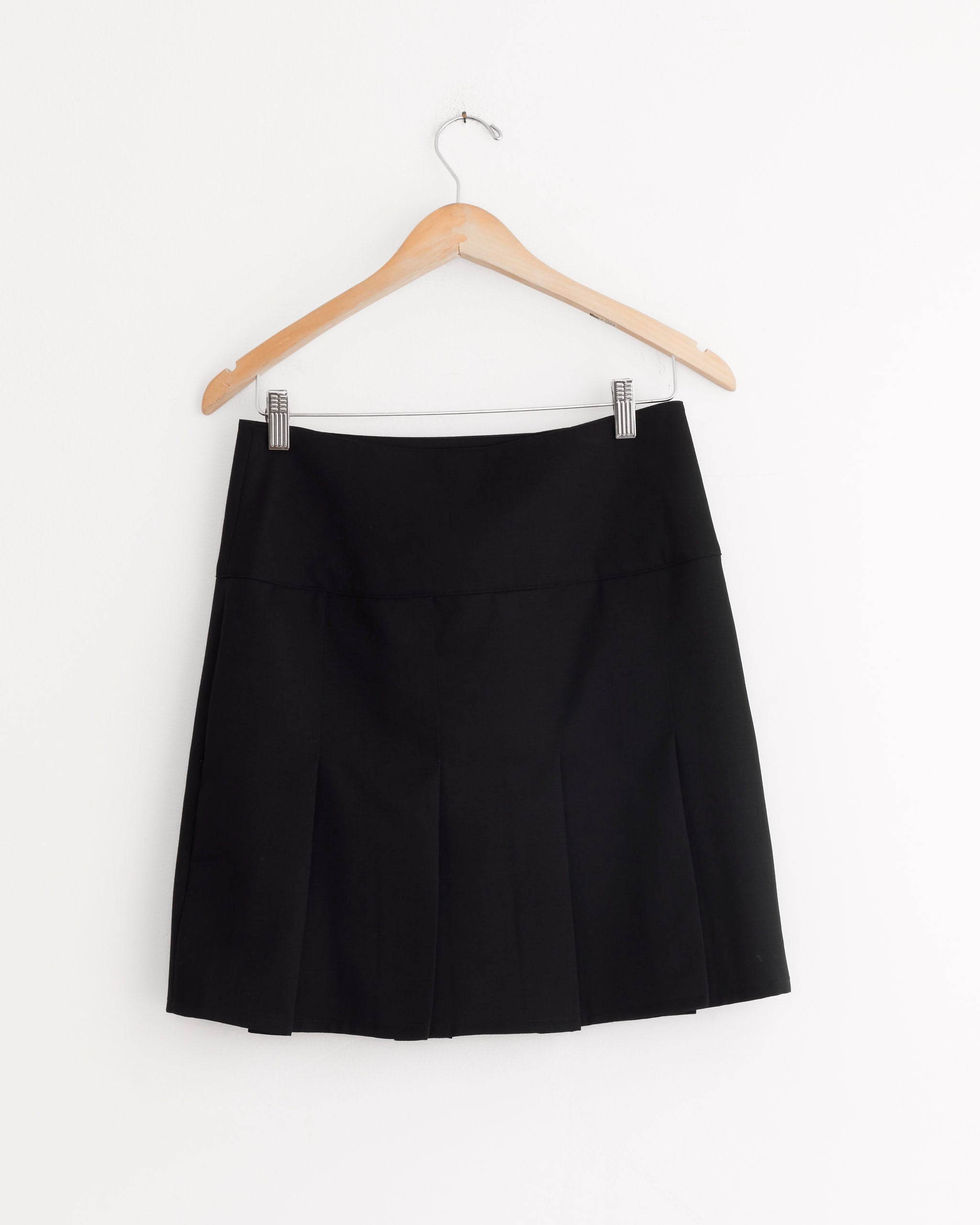 The Girdle Skirt in Coarse Black Gabardine by Our Legacy hangs on a wooden hanger against a white background, highlighting its classic A-line silhouette.
