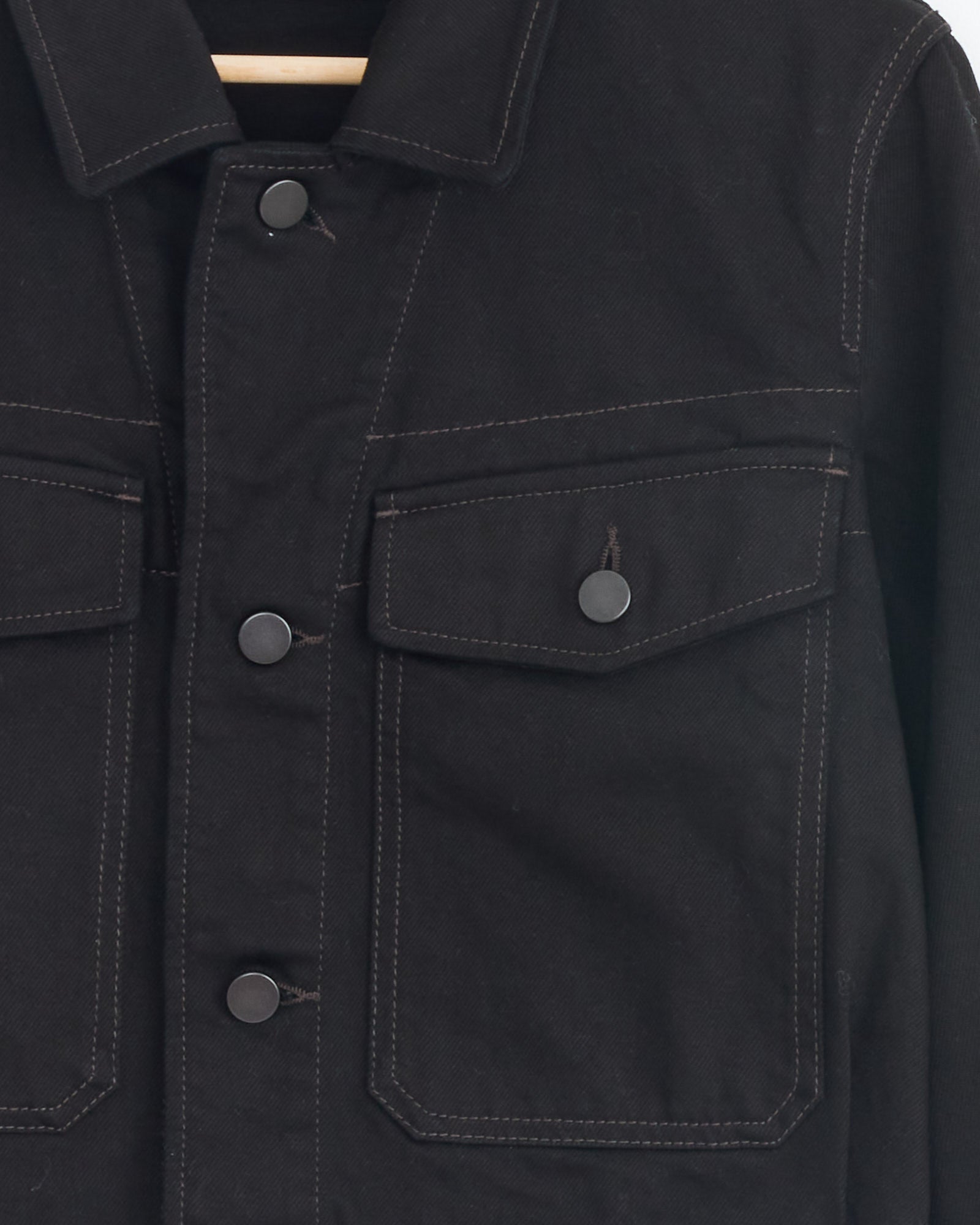 Close-up of the Lemaire Cropped Blouson in Black, showcasing its workwear-inspired design with two flap chest pockets, snap buttons, visible stitching, and parts of the collar and sleeve.