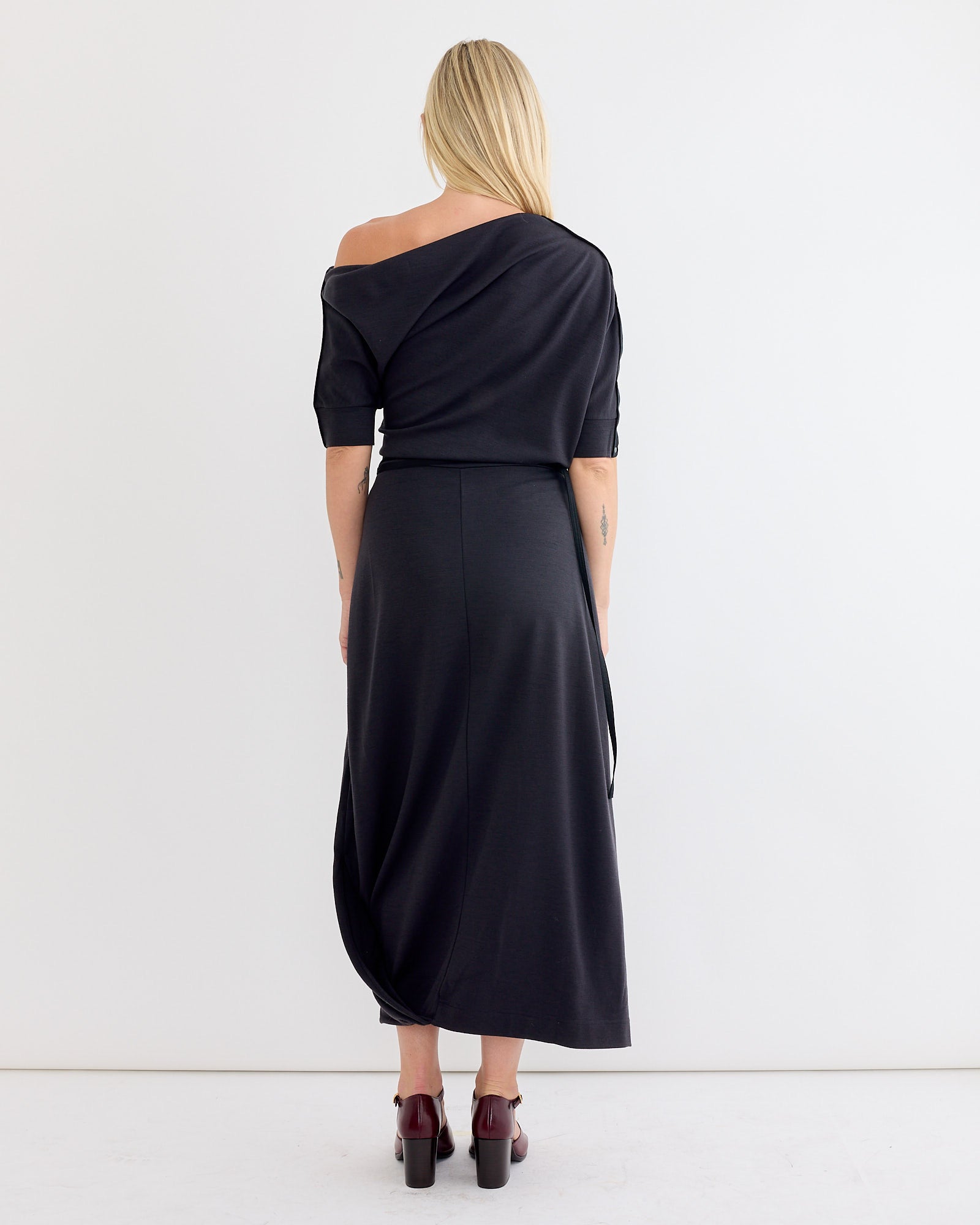 A woman in the Lemaire Twisted Hem Dress in Anthracite, featuring an asymmetrical neckline.