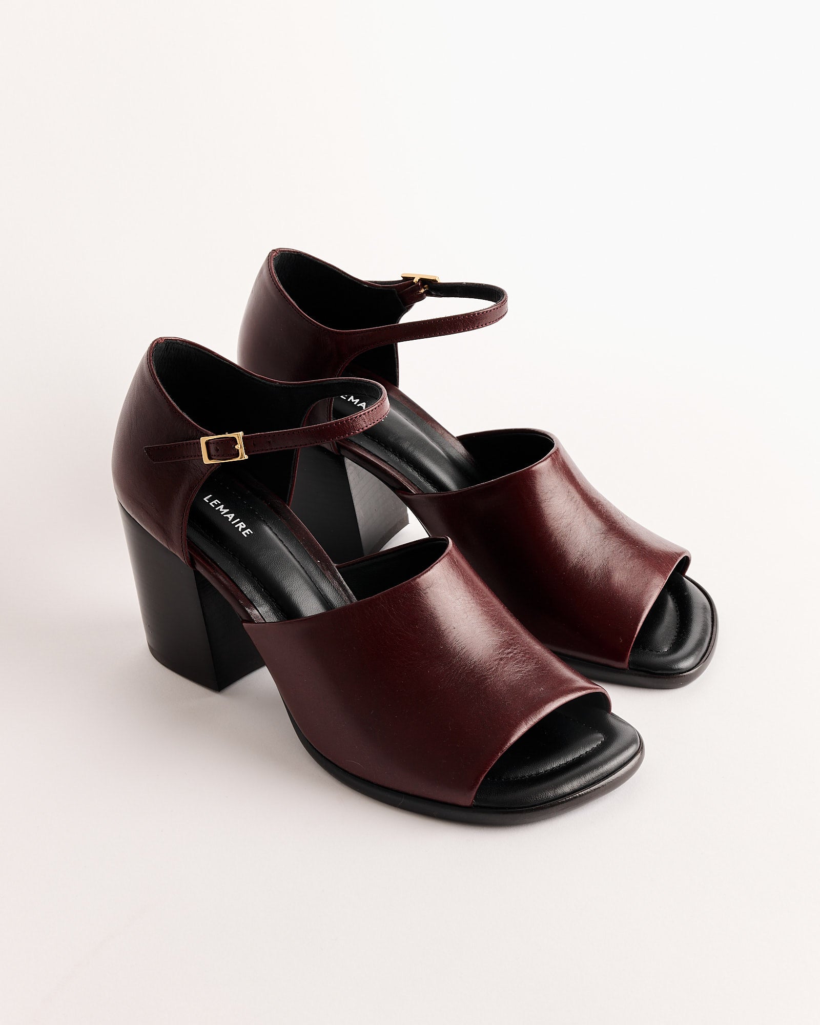 The Lemaire Square Heeled Sandal in Chianti features maroon vegetable-tanned leather, open toes, block heels, ankle straps with gold buckles, and is shown on a white background.