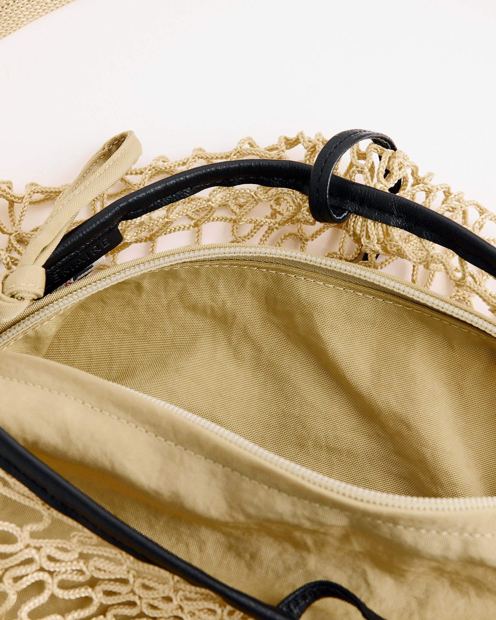A close-up of the Lemaire Fortune Croissant Filt Bag in Light Beige, featuring fabric lining and black leather handles, displayed on a light background.