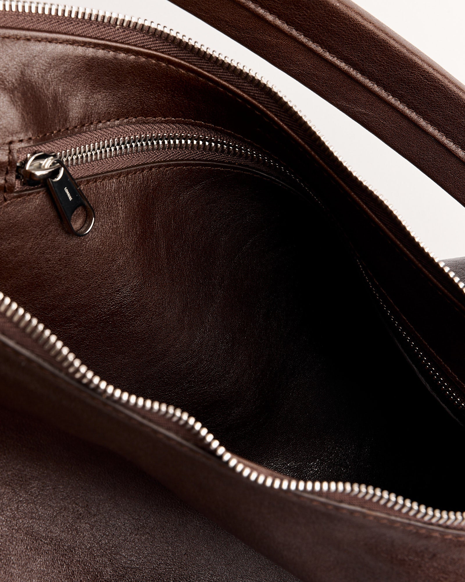 Close-up of the interior of the Lemaire Belted Hobo Bag in Espresso, featuring a main compartment and a zippered inner pocket with a silver zipper.