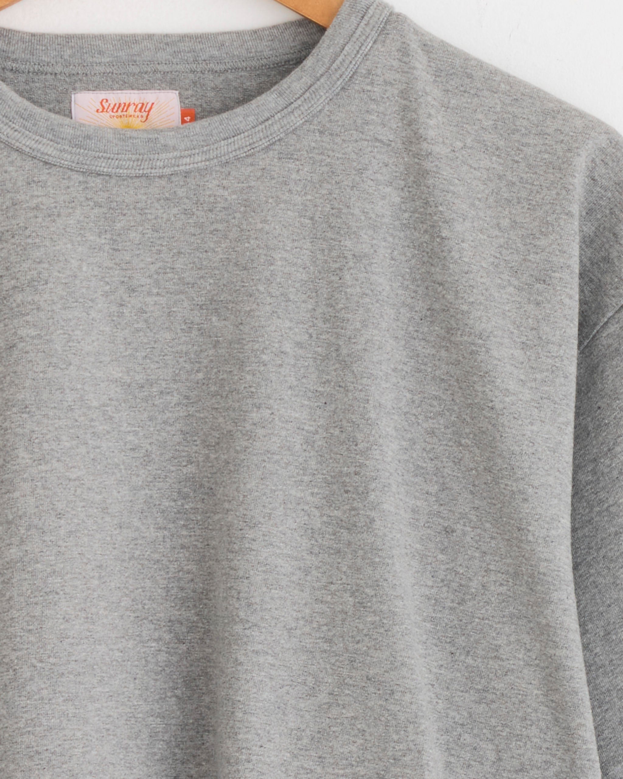 A close-up of the Sunray Makaha Japanese Jersey T-Shirt in Hambledon Grey hangs on a wooden hanger against a white background, focusing on the upper chest, neckline, sleeve, and a "made in Japan" tag inside the collar.