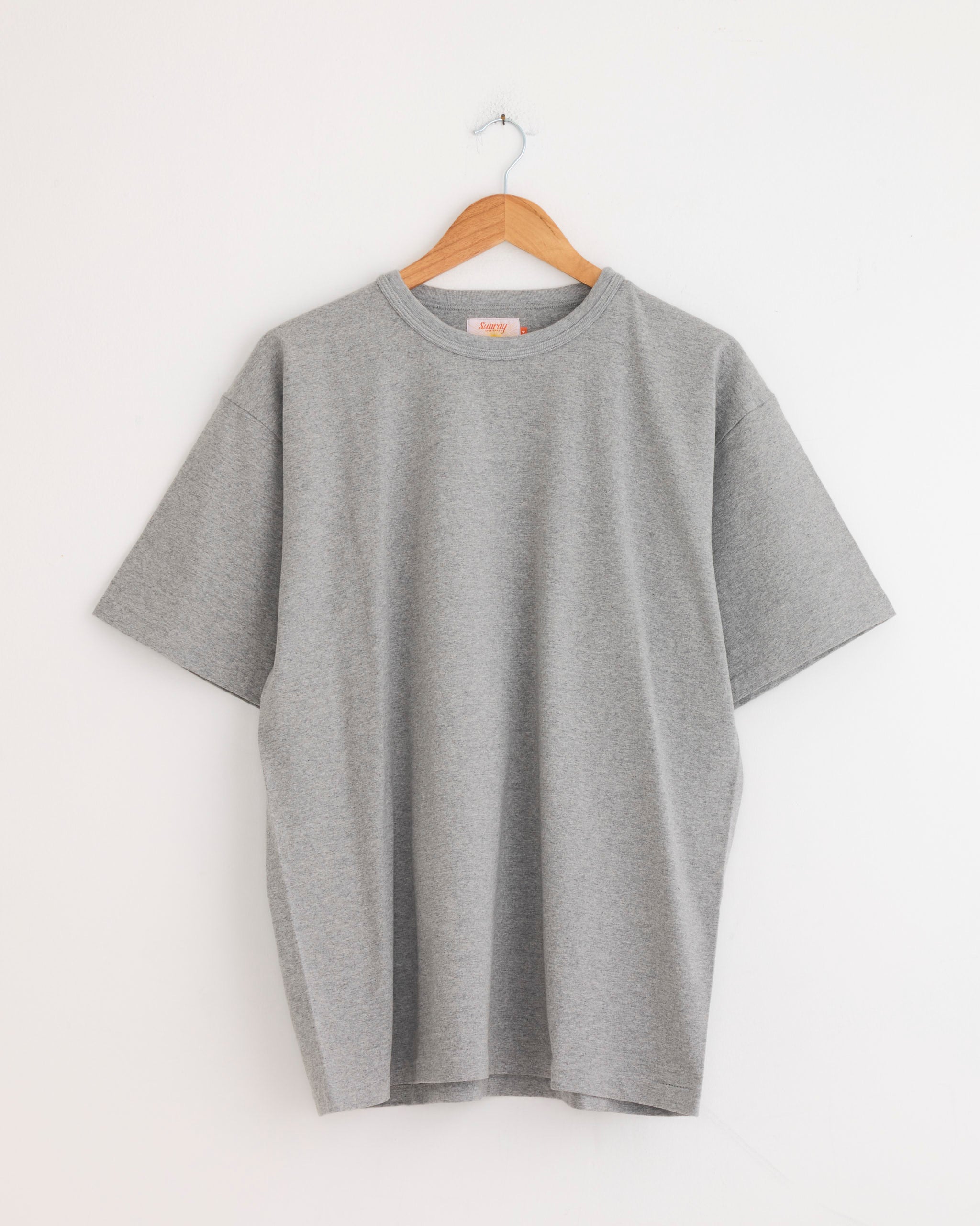 The Sunray Makaha Japanese Jersey T-Shirt in Hambledon Grey hangs on a wooden hanger against a white wall.