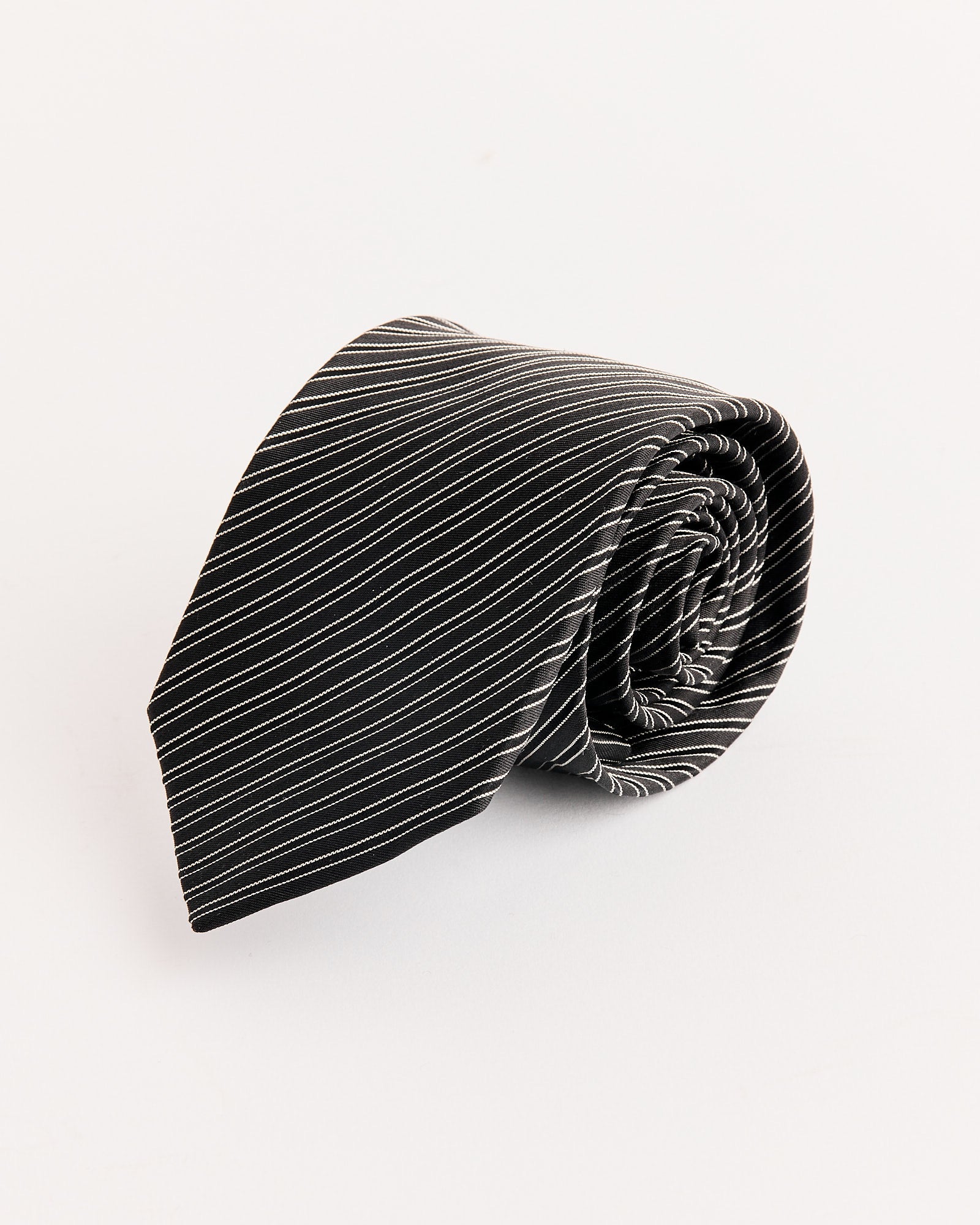 The mfpen Banquet Tie in Black Fine Stripe features thin white diagonal stripes and a subtle jacquard pattern, shown rolled up on a plain white background.