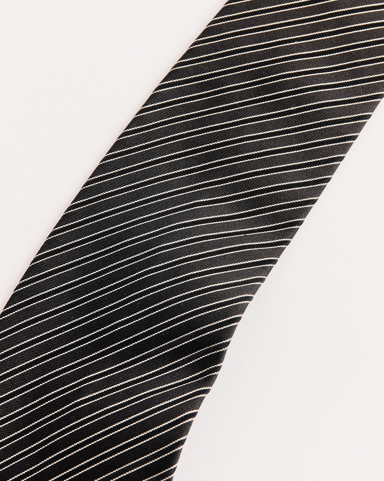 A close-up of the mfpen Banquet Tie in Black Fine Stripe, featuring thin white diagonal stripes and a subtle jacquard pattern, set against a plain white background.