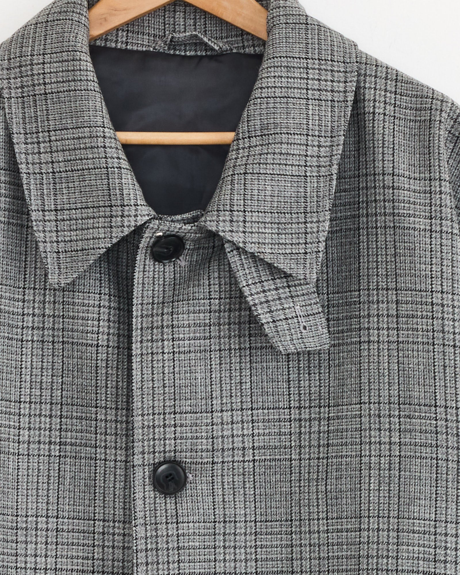 A close-up of the mfpen Client Coat in Grey Glen Check, displayed on a wooden hanger against a plain white background.