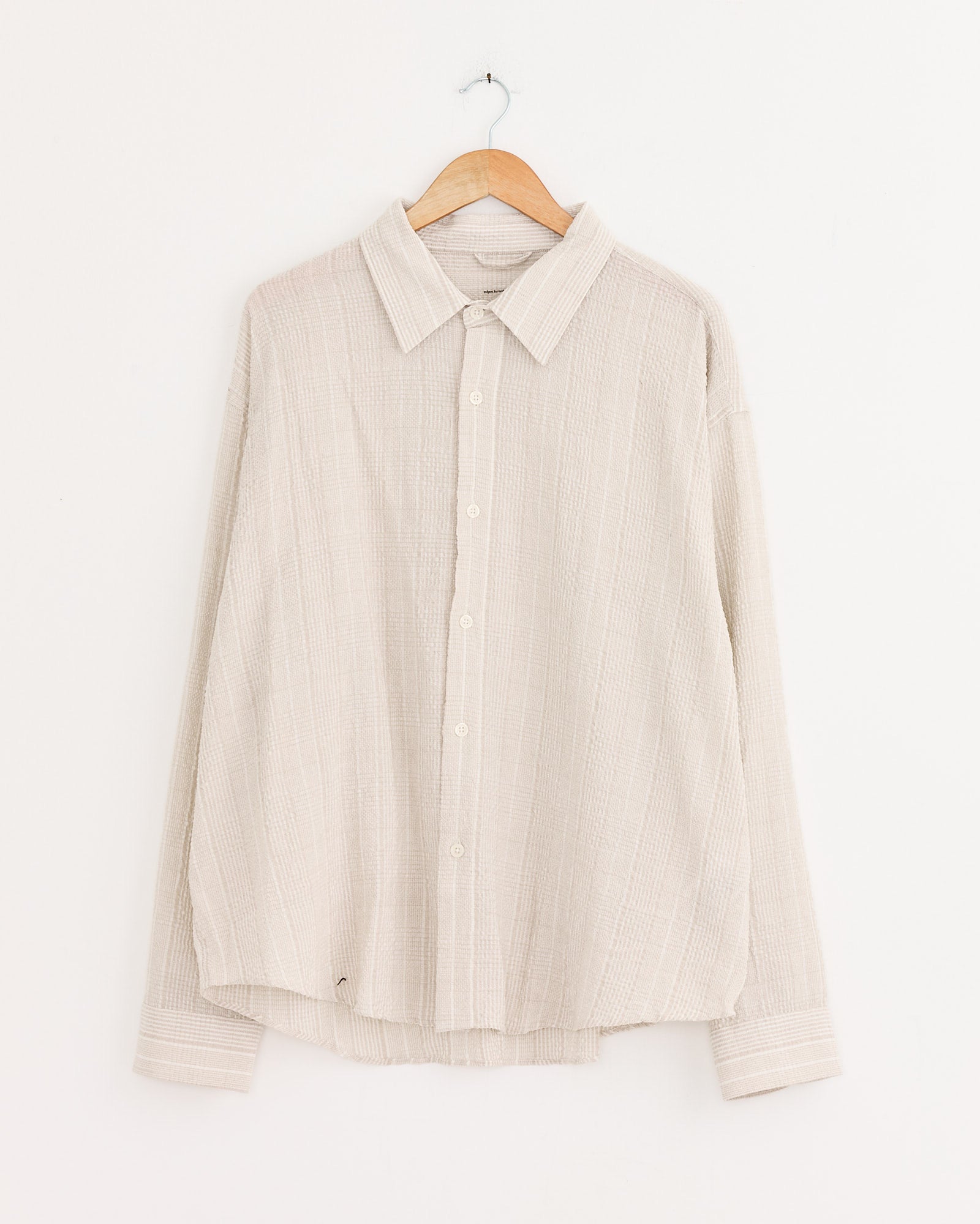 A beige mfpen Exact Shirt in Dusty Seersucker Check with subtle stripes hangs on a wooden hanger against a white background.