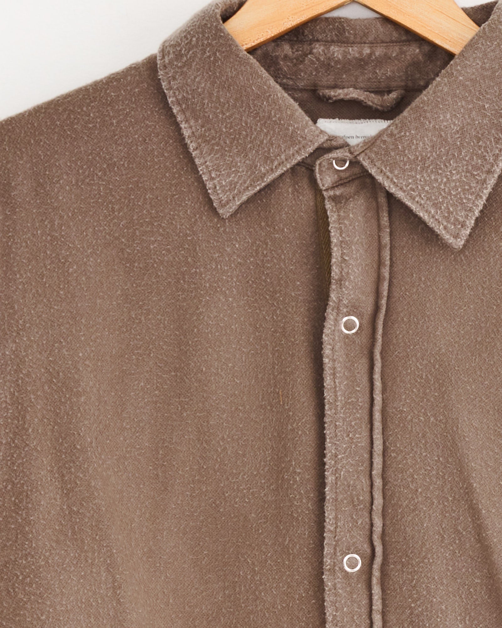 A close-up of the oversized mfpen Gambler Shirt in Dark Taupe Fuzz on a wooden hanger, highlighting its brown textured fabric, snap buttons, and pointed collar.