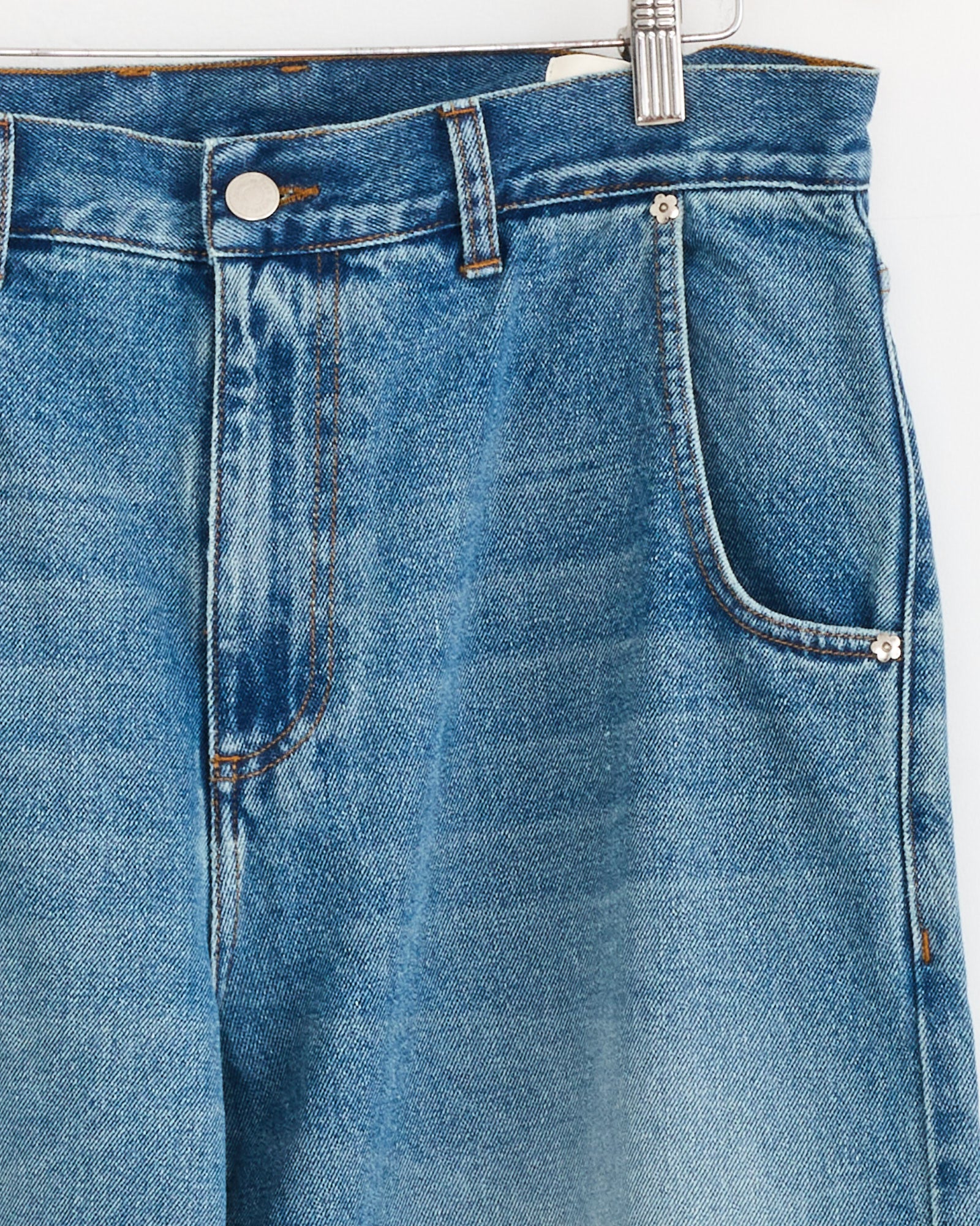 Close-up of the mfpen Straight Cut Jean in Vintage Blue on a hanger, highlighting the waistband, button, zipper, belt loops, and front pockets with visible orange stitching.