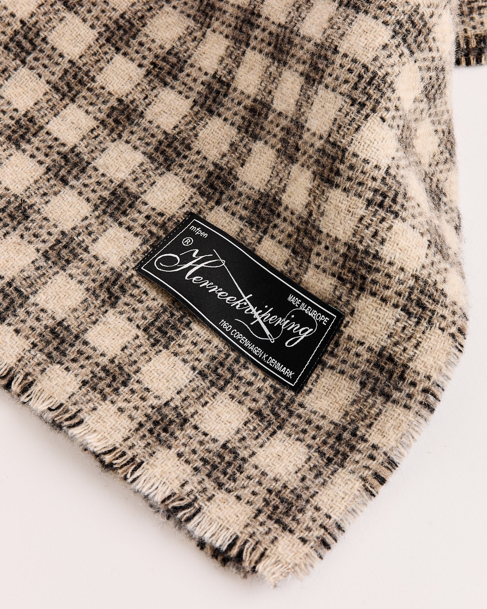 A grey double-faced check wool scarf by mfpen with slightly frayed edges and a black and white woven label noting 100% Copenhagen, Denmark.