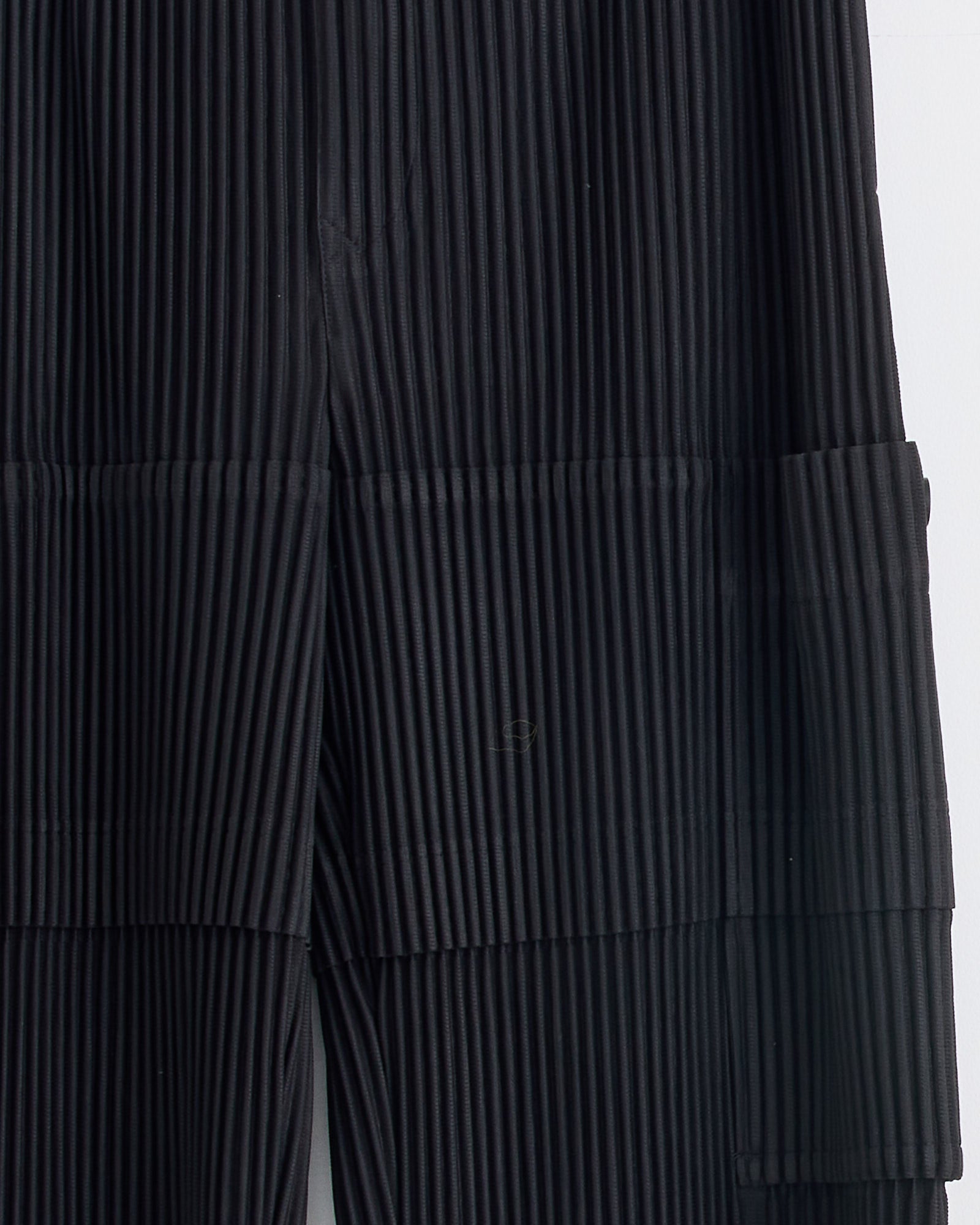 Close-up of pleated Coke Grey fabric with vertical and horizontal lines, creating texture. Visible seams and structured folds show the tailored fit of the Homme Plissé Issey Miyake Multi Pocket Pant.