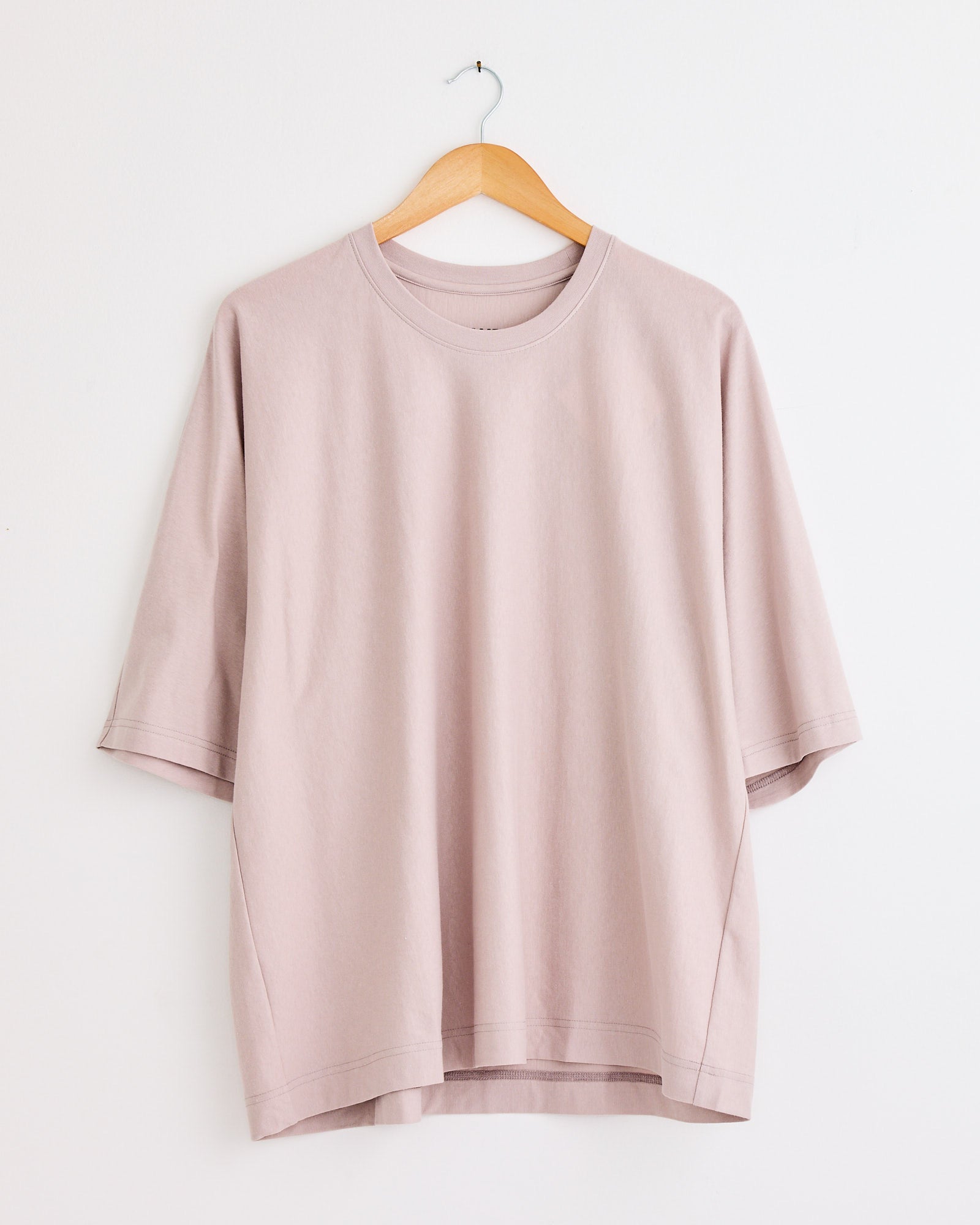 The Homme Plissé Issey Miyake Release T1 T-Shirt in Purple Grey hangs on a wooden hanger against a white wall—contact online chat for sizing and fit help.