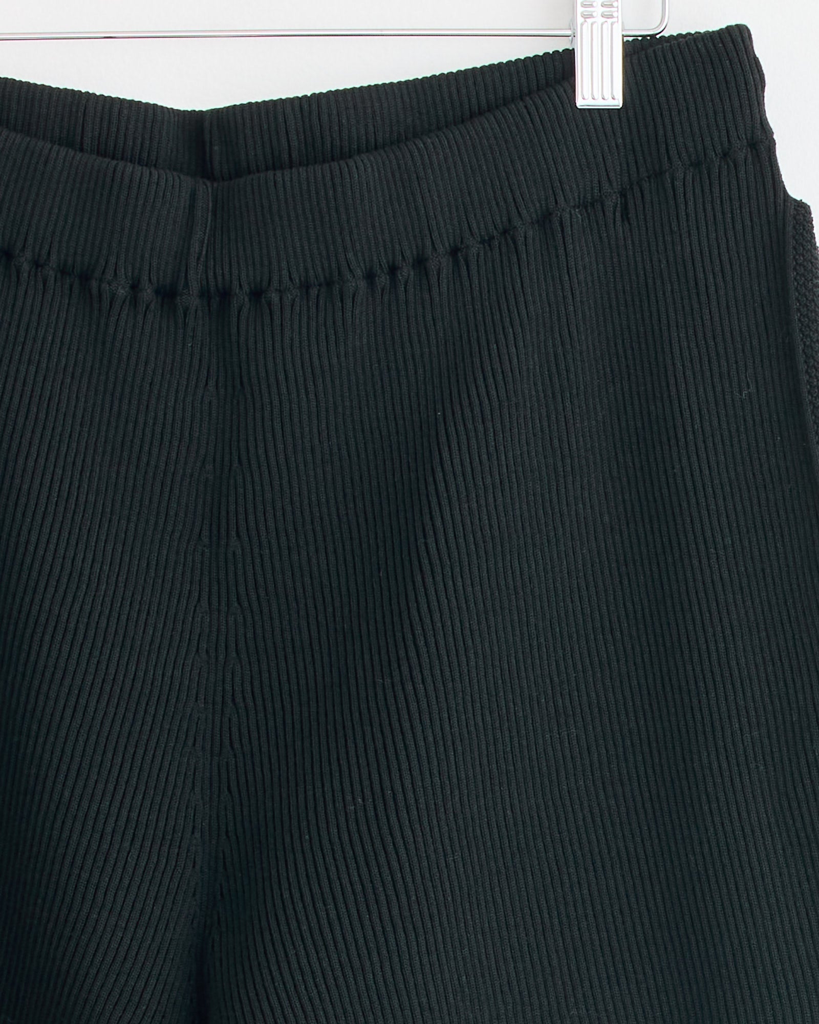 Close-up of the waistband and upper section of the Homme Plissé Issey Miyake Basic Knit Pant in Black, displayed on a hanger against a white background—ideal for viewing fit and sizing details before purchase.