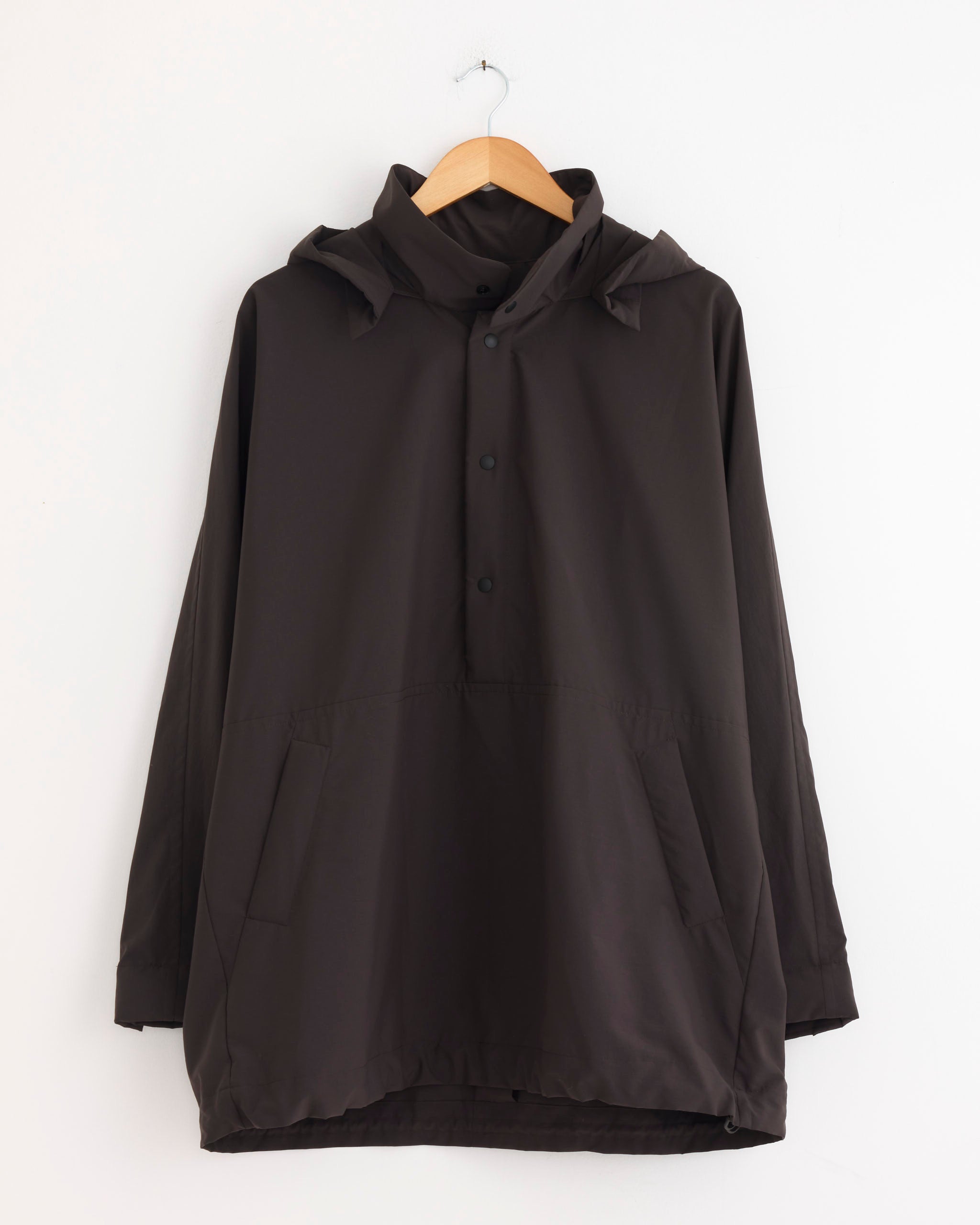 The Padded Rim Shirt in Brown by Homme Plissé Issey Miyake, featuring a pleated design with snap buttons and front pockets, hangs on a wooden hanger against a white background.