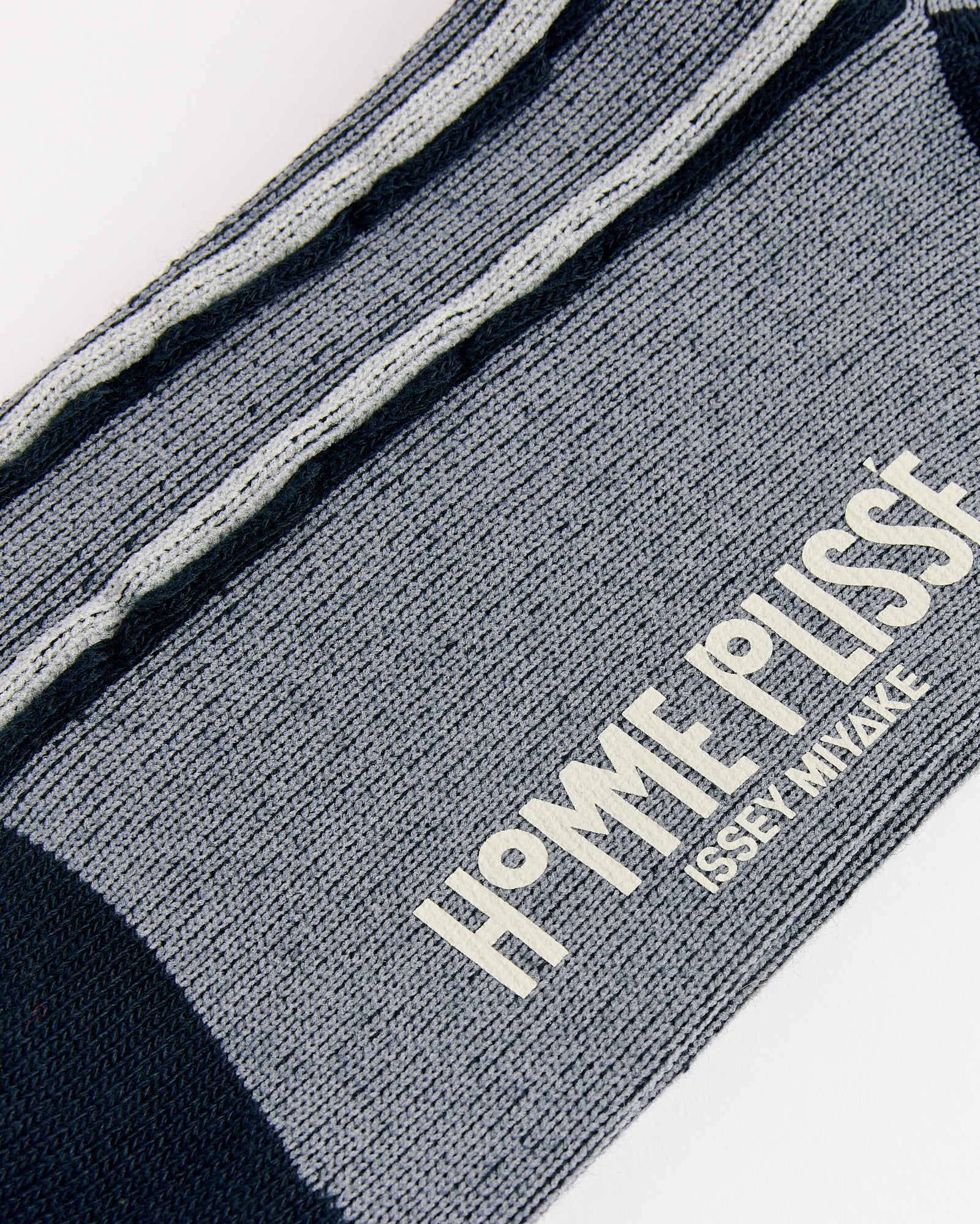 Close-up of the Masonry Sock in Black by Homme Plissé Issey Miyake—gray and black textured fabric with white embroidered branding, highlighting the innovative design and Japanese craftsmanship of these premium socks.