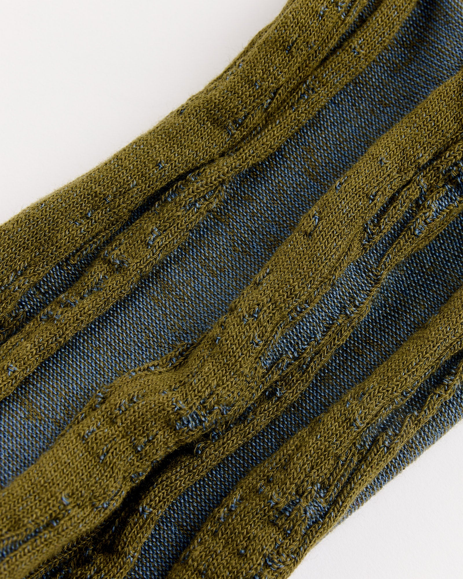 A close-up of olive green knitted fabric with an intricate pattern over blue denim, echoing the craftsmanship of IM MEN's Cotton Jacquard Socks in Green, made in Japan.