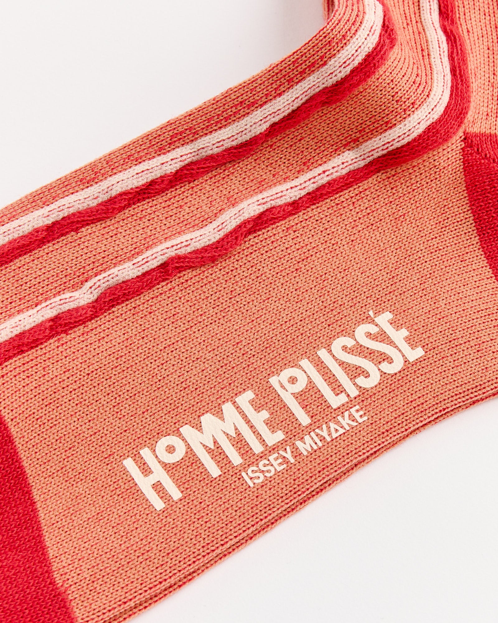 Close-up of the Masonry Sock in Red by Homme Plissé Issey Miyake, showcasing bold white text near the ankle and a striking red and pink Japanese cotton design.